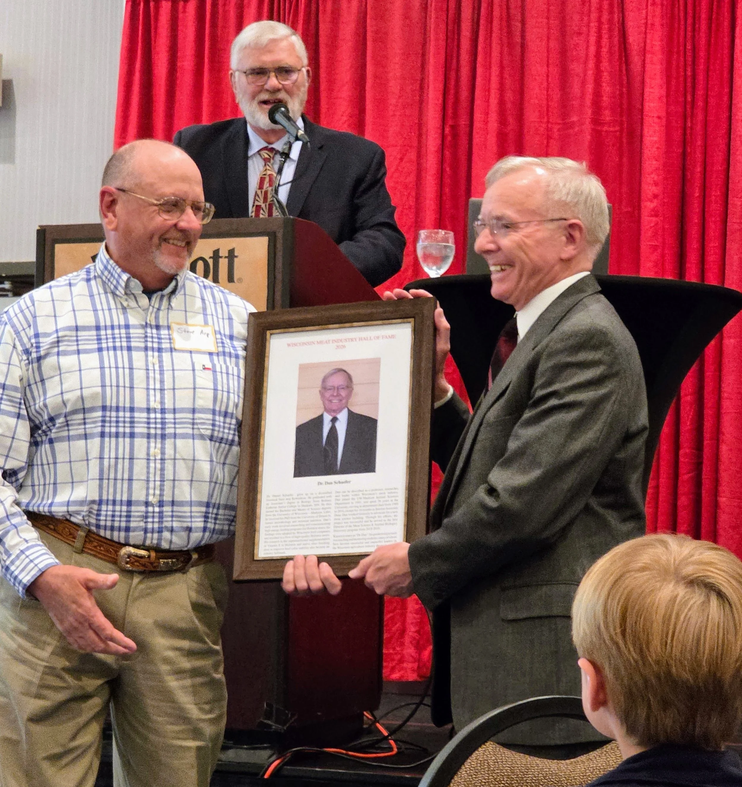 Jerry Huth stands at the podium after having read the Hall of Fame citation for Dan Schaefer. Steve Arp is presenting the commemorative plaque to Dan Schaefer.
