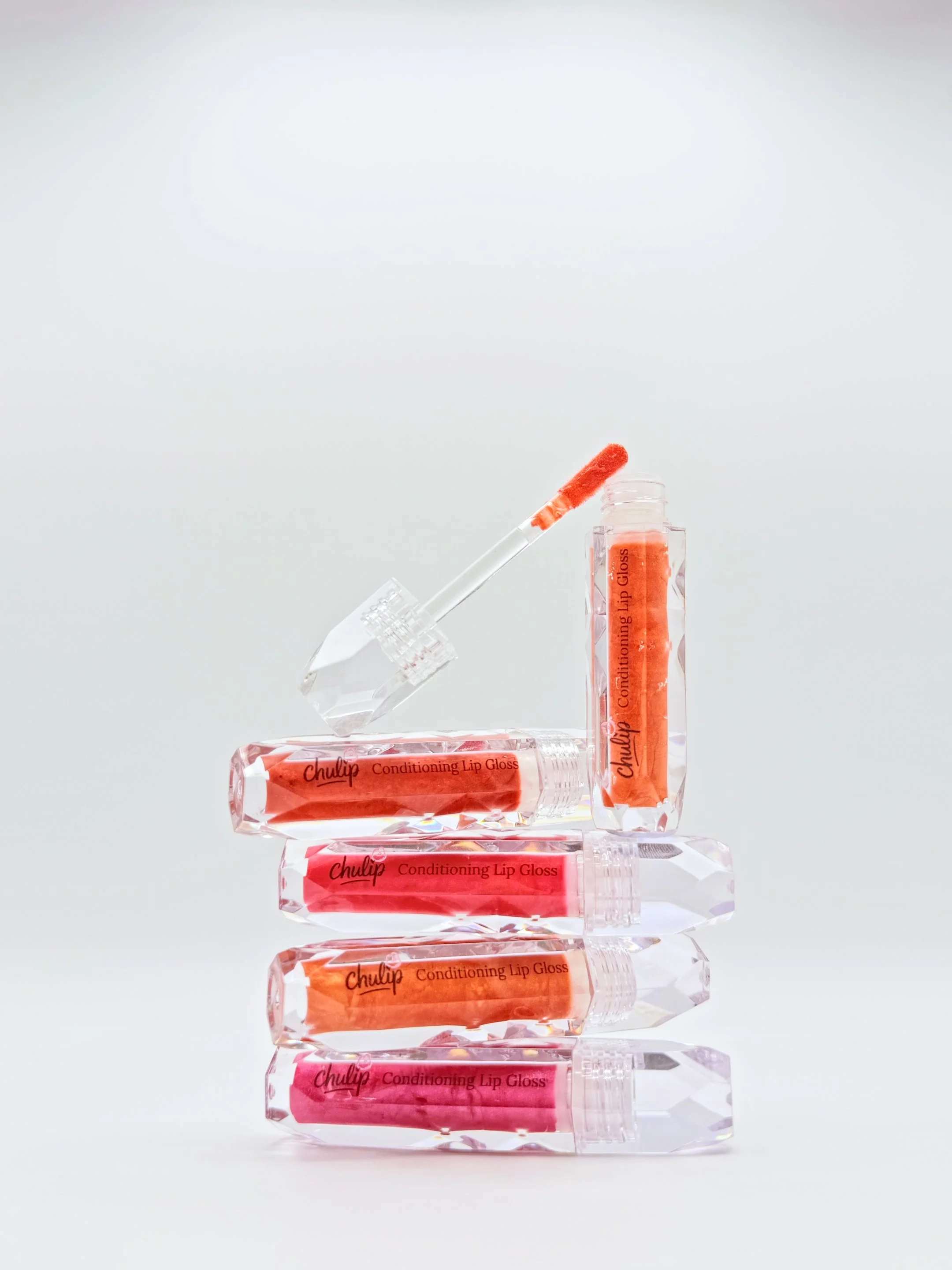 A stack of five tubes of CHULIP Conditioning Lip Gloss with orange and pink shades, arranged vertically on a reflective surface against a plain background.