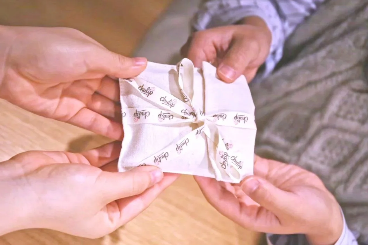 One person is handing over the cute CHULIP ribbon cotton bag to the other.