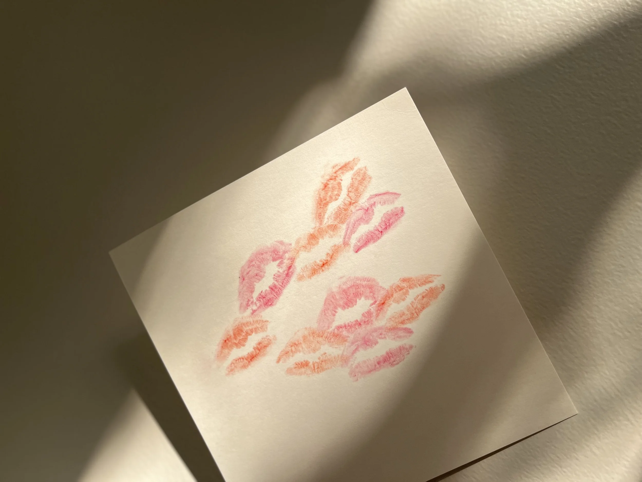 Kiss marks on a white piece of paper with pink and orange lipsticks/tinted lip balms.