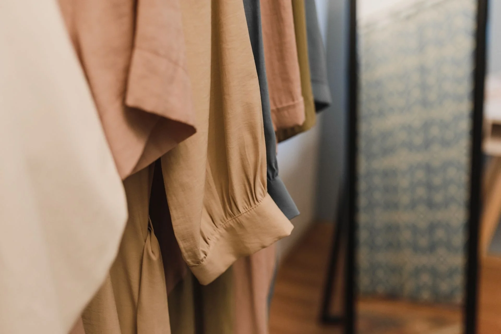 Clothes hanging on a rack, including beige, gray, and patterned garments