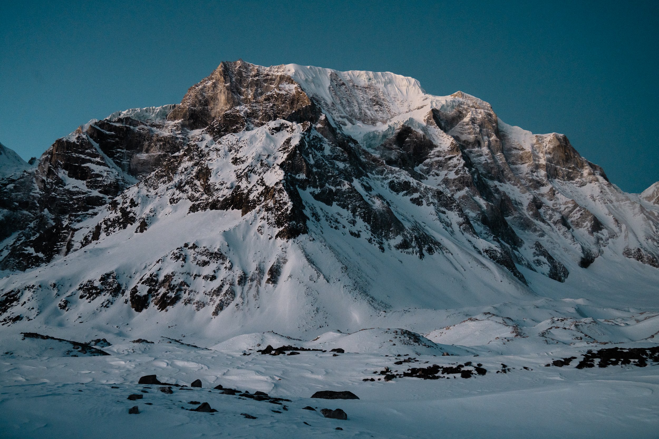 Snow-covered mountain with rocky peaks under a clear sky.