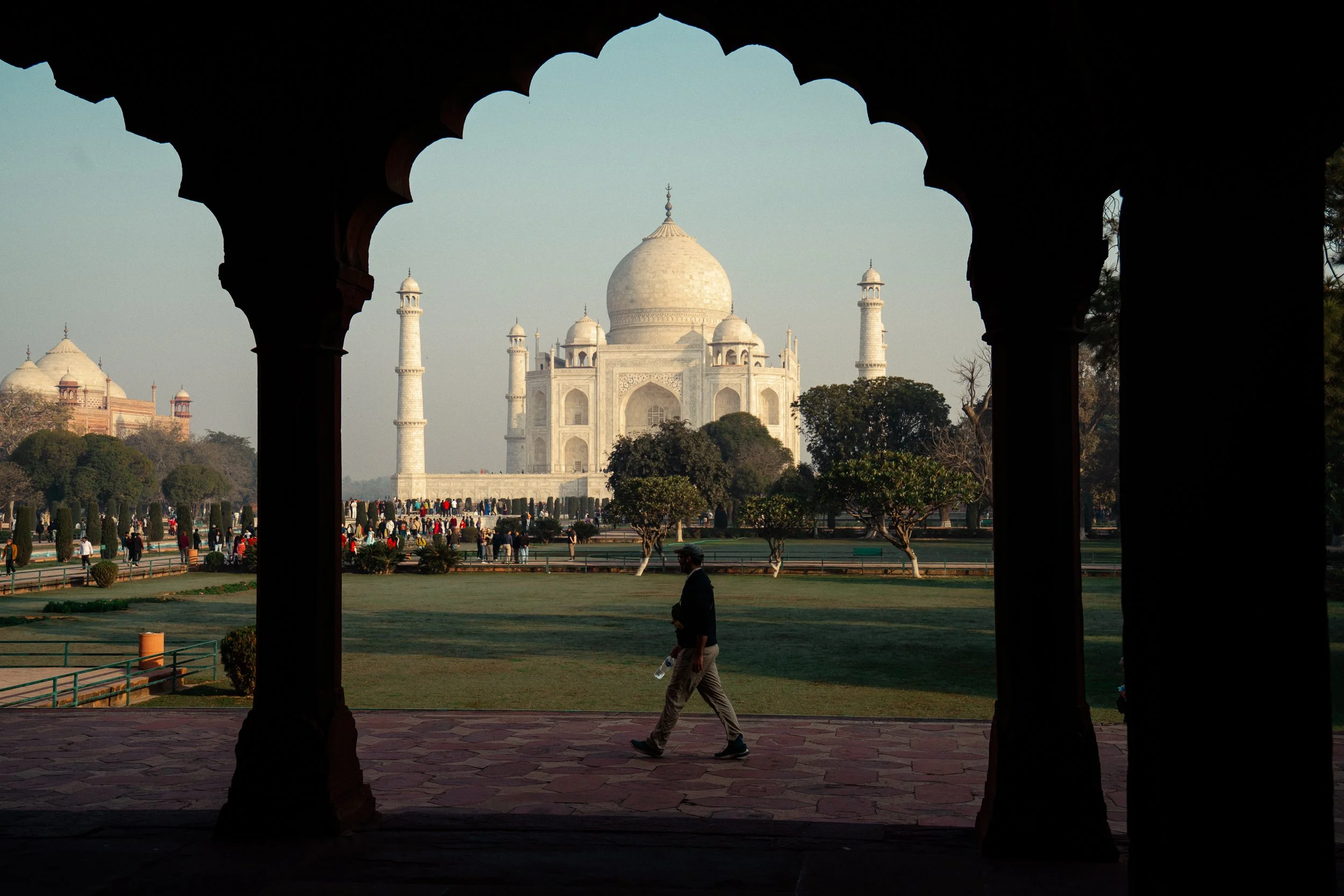 View of the Taj Mahal framed by the arches of a nearby building with people walking in front.