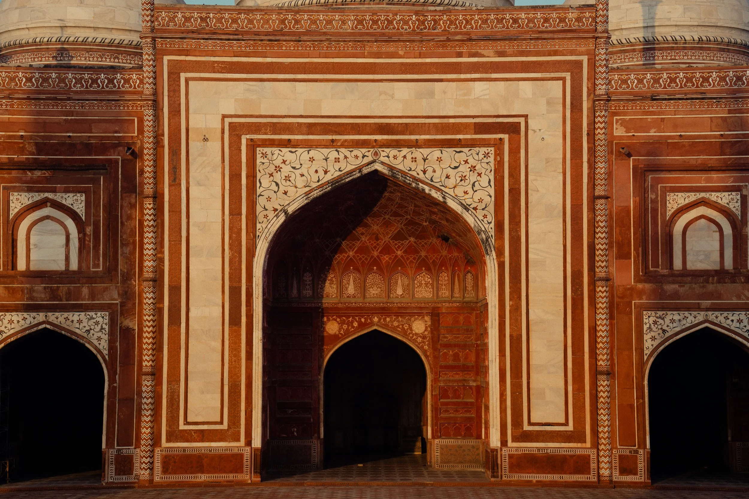 Close-up view of intricate marble and inlay work on an Indian architectural structure, showcasing archways and detailed patterns with earthy tones of red, white, and black.