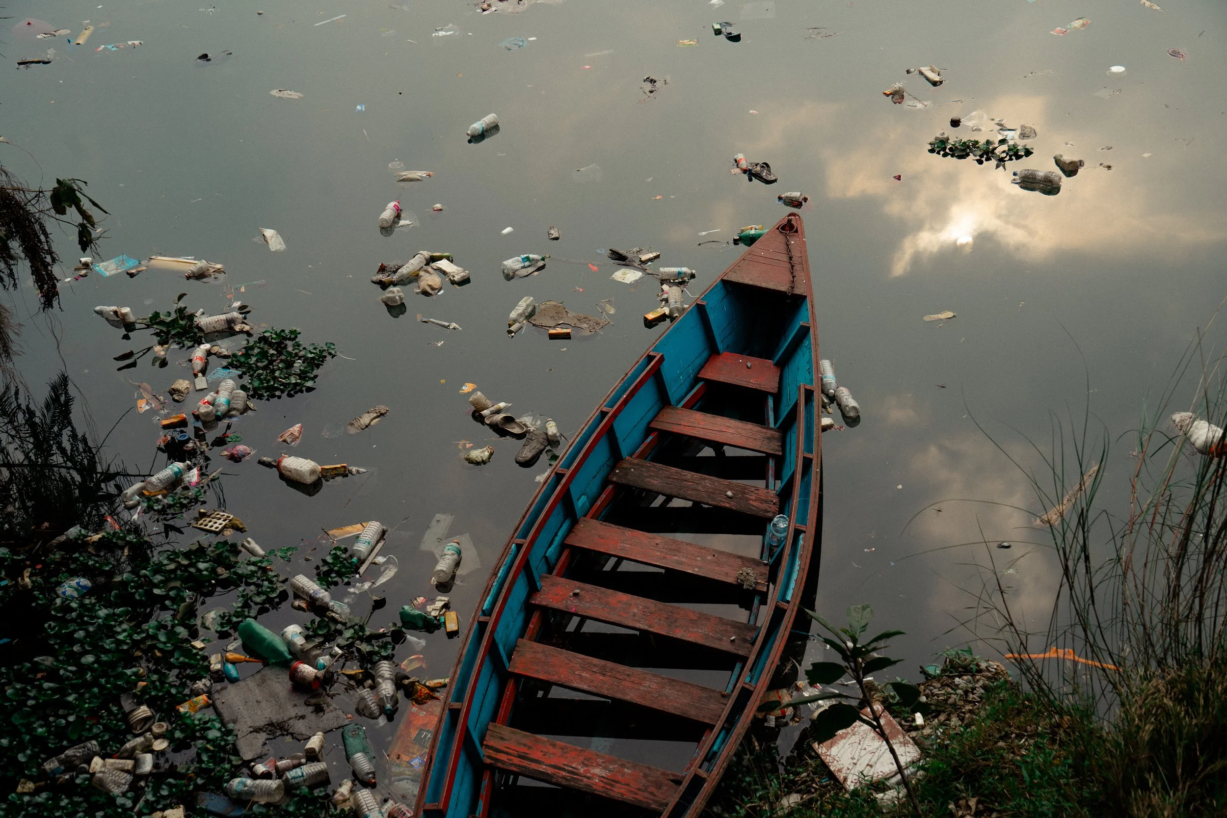 A boat in a polluted body of water filled with floating trash, including plastic bottles and debris.