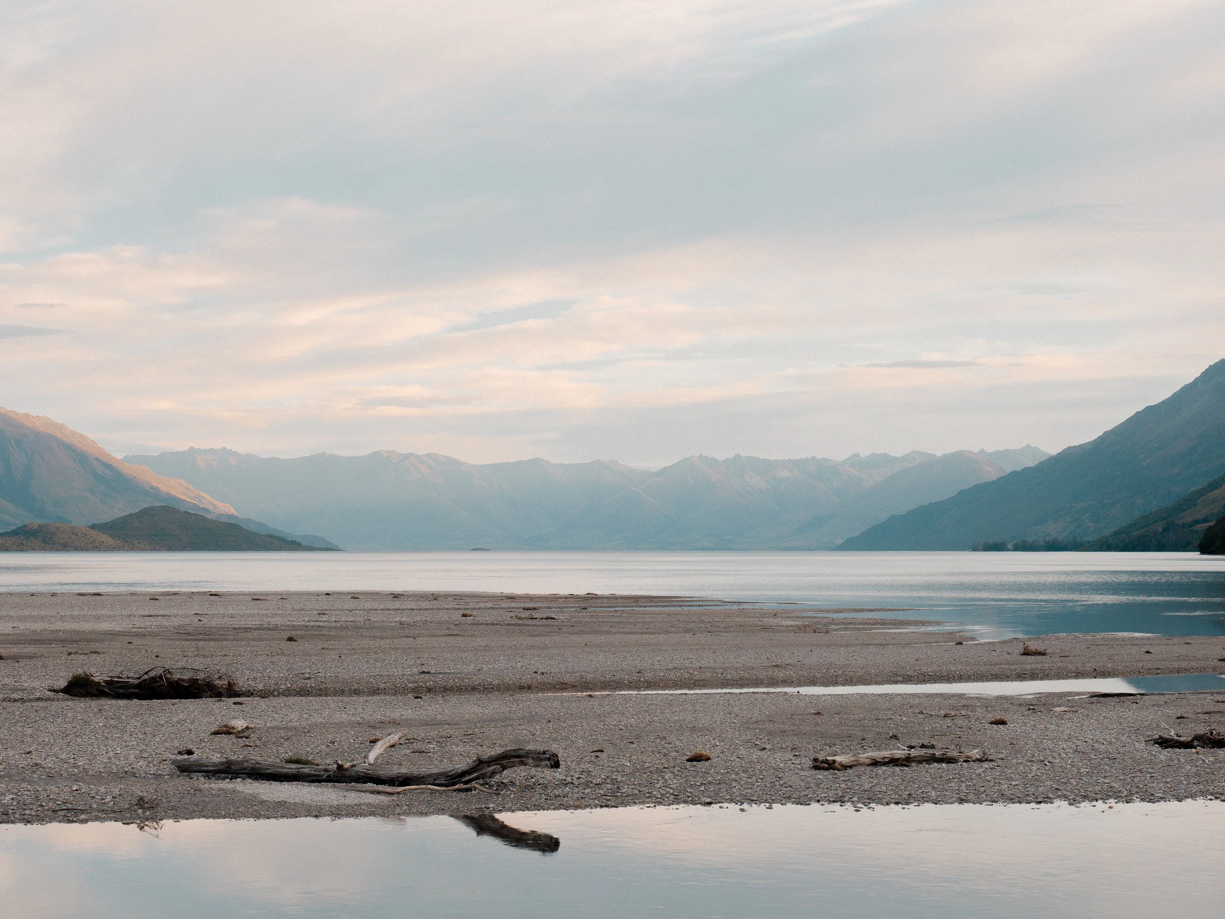 View of a tranquil lake surrounded by mountains with a partly cloudy sky overhead.