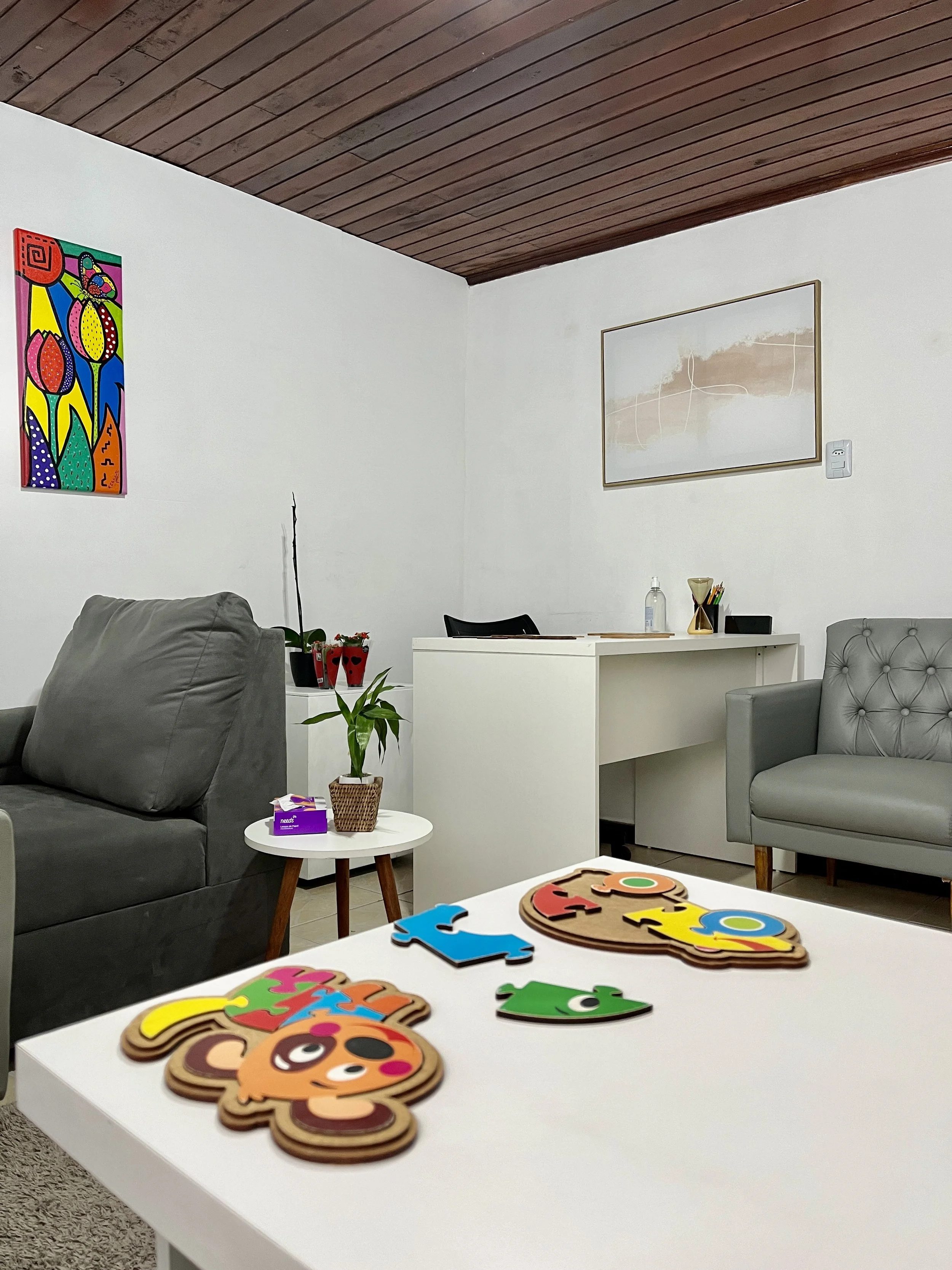 Consultório de psicologia, com mesa de atendimento, poltronas, e mesa para jogos com crianças