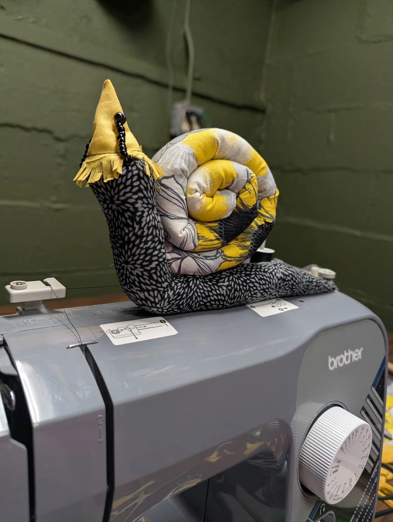 Close-up of a sewing finger with a fabric-covered spiked thimble attached, placed on top of a Brother sewing machine.