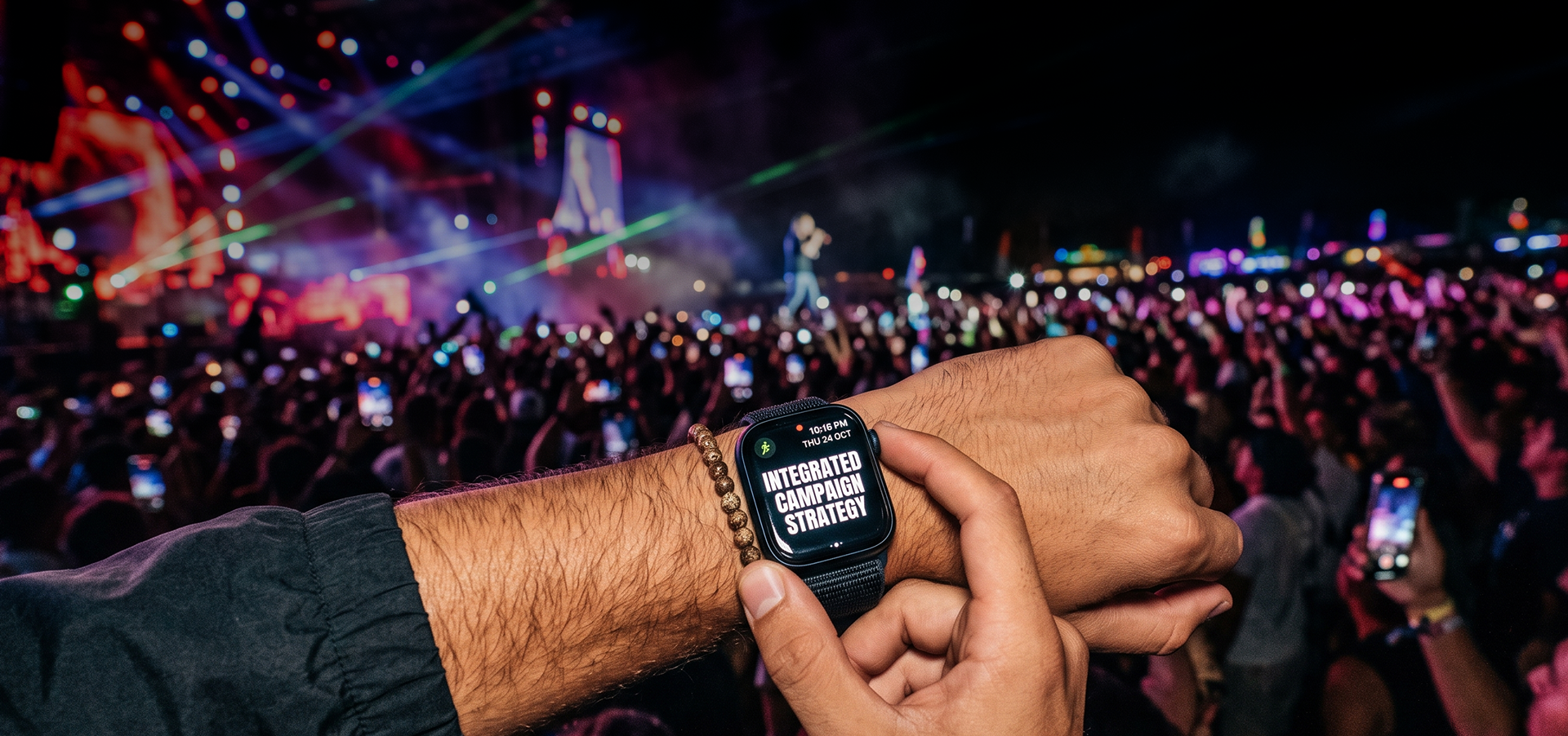 Person checking a smartwatch displaying 'Integrated Campaign Strategy' at a crowded concert or event with a large stage and audience in the background.