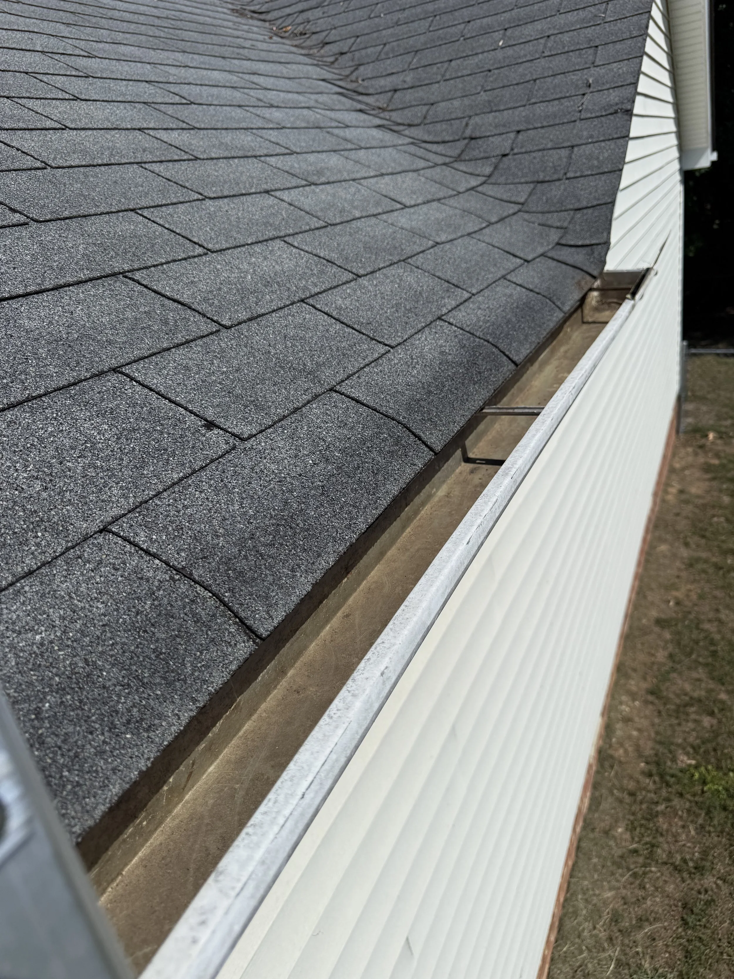 Close-up view of a roof with asphalt shingles and a gutter on the side of a house. Gutter has been cleared of all debris.