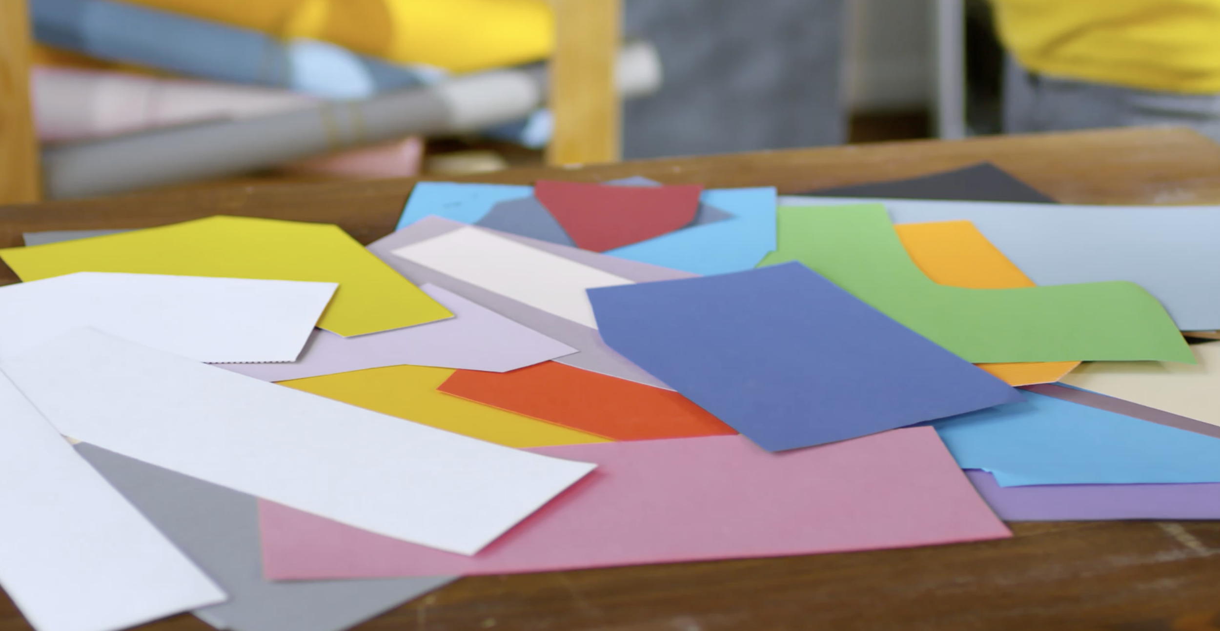 Colorful paper sheets scattered on a table with a blurred background of shelves and chairs.