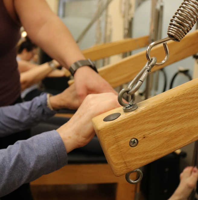 People practicing Pilates on wooden reformer machines in a fitness studio.