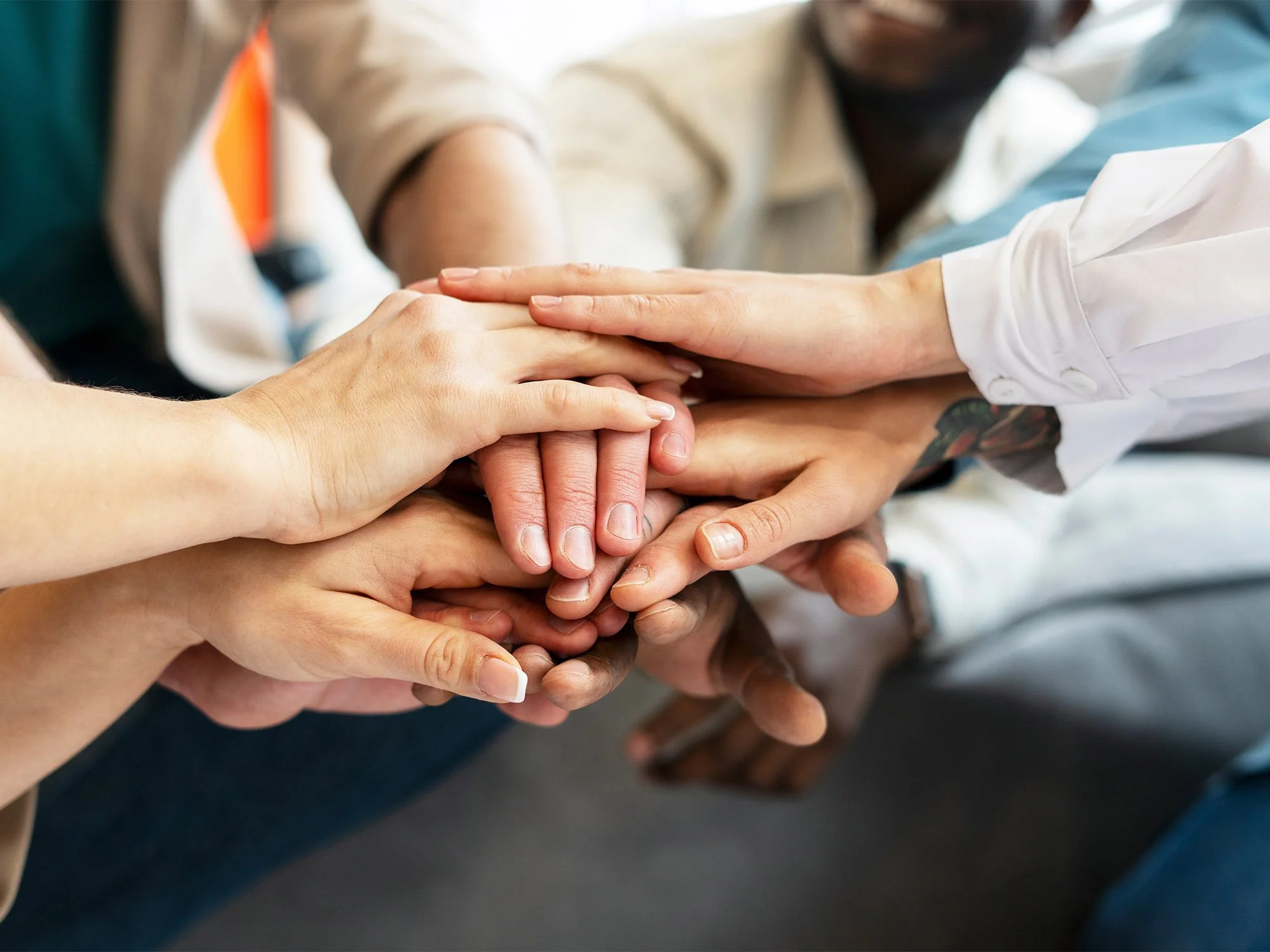 Multiple hands of diverse individuals stacked together, symbolizing teamwork and unity.