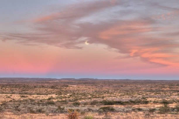 A vast desert landscape under a colorful sunset sky with pink and purple clouds.