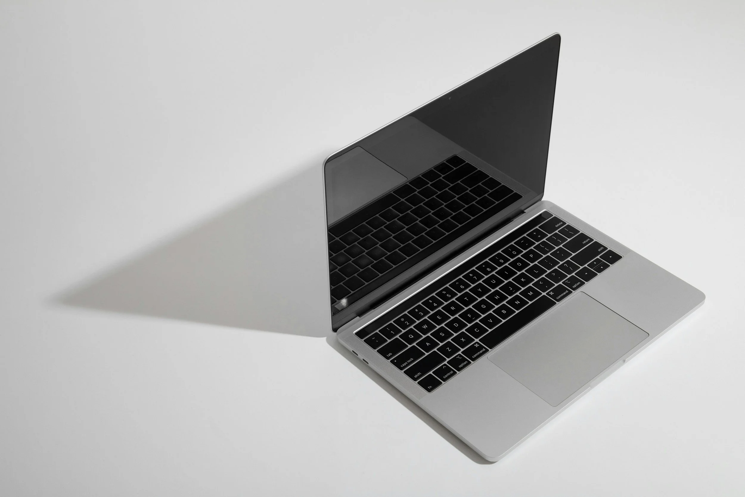 A silver laptop with a black keyboard open on a white surface, viewed from above.