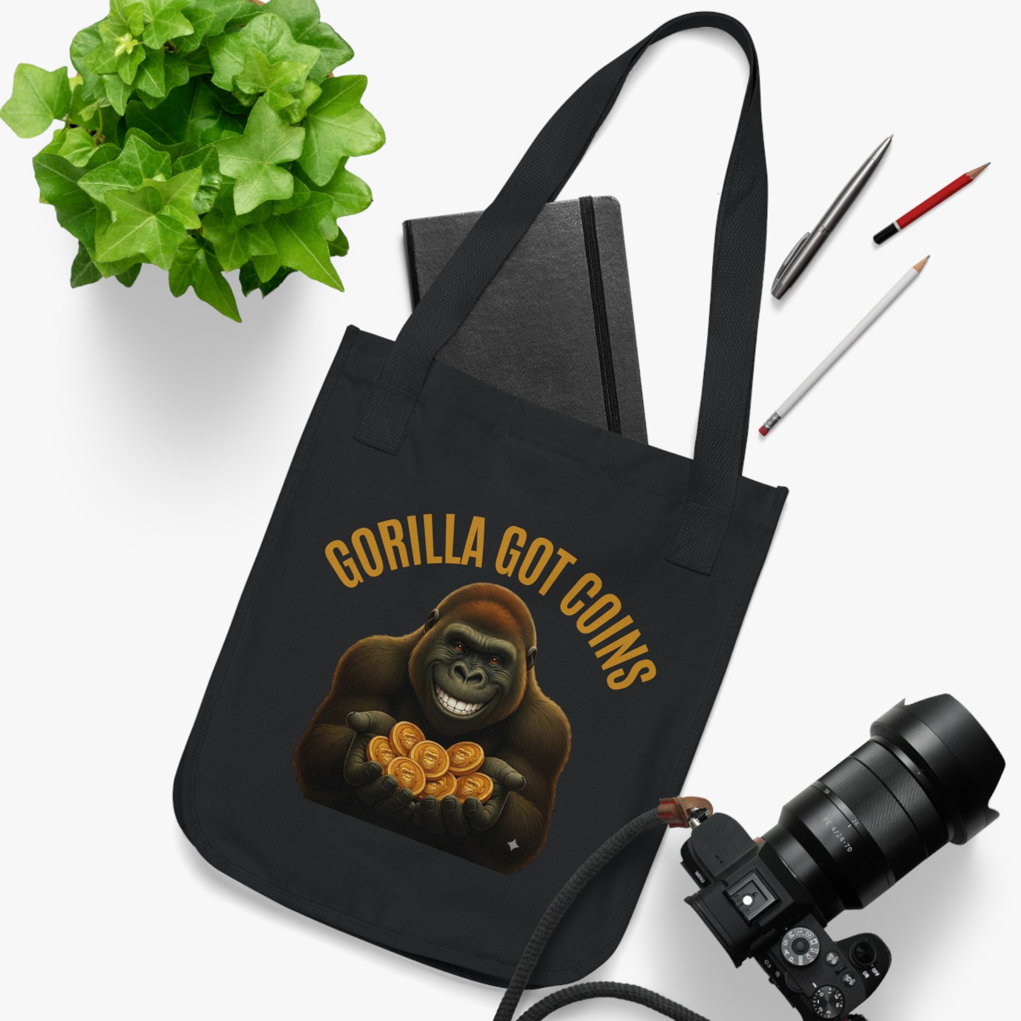 Green ivy plant, black camera bag with yellow text, two pencils, and parts of a camera on a white background.