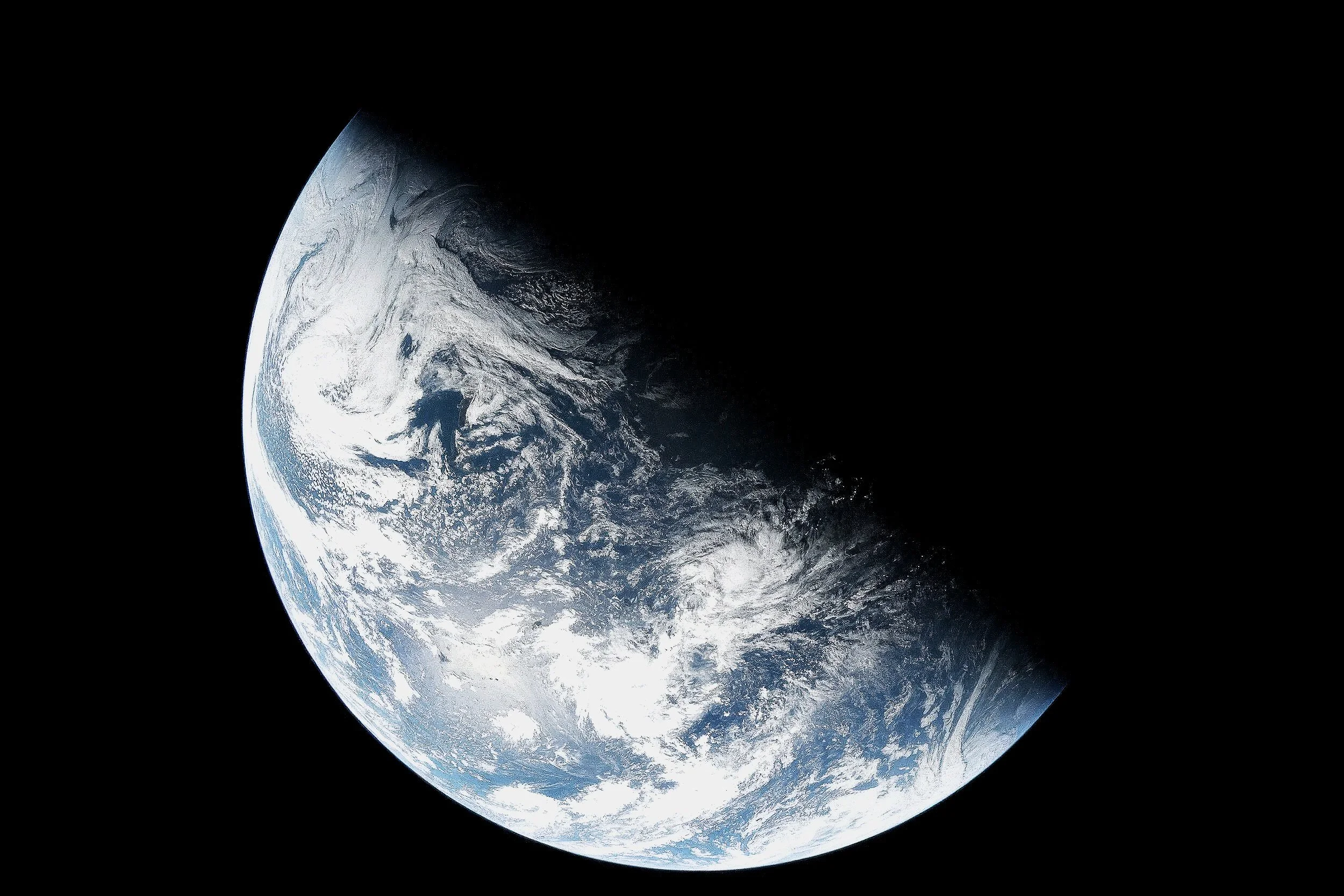 A view of the Earth from space, showing the planet's curvature with swirls of clouds across its surface, set against the blackness of space.