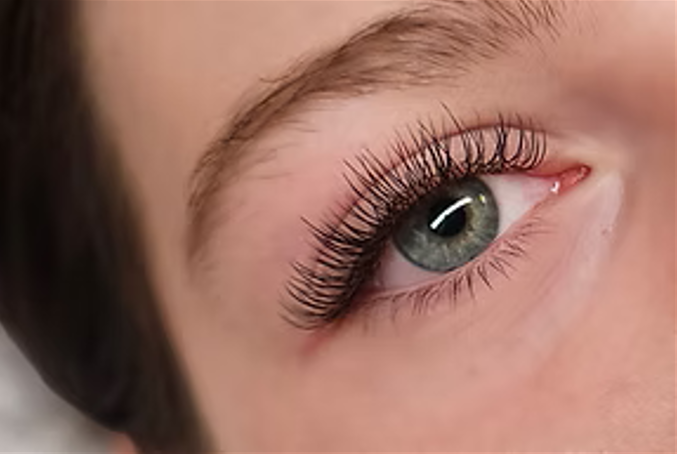 Close-up of a person's eye with long, curled eyelashes and light-colored eye makeup.