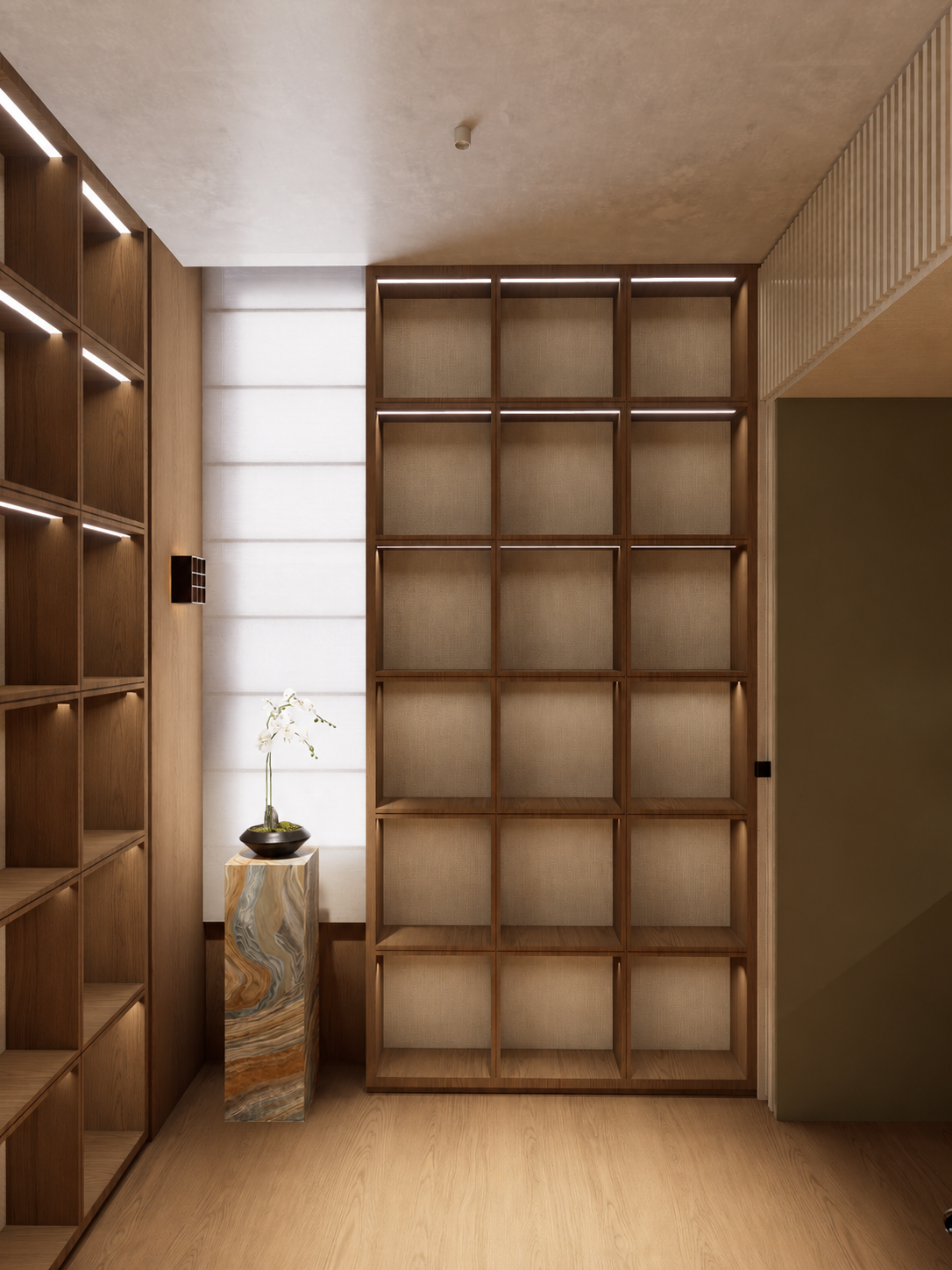 A room with wooden shelving units and a small vase with white flowers on a marble stand, illuminated by natural light from a window with blinds.