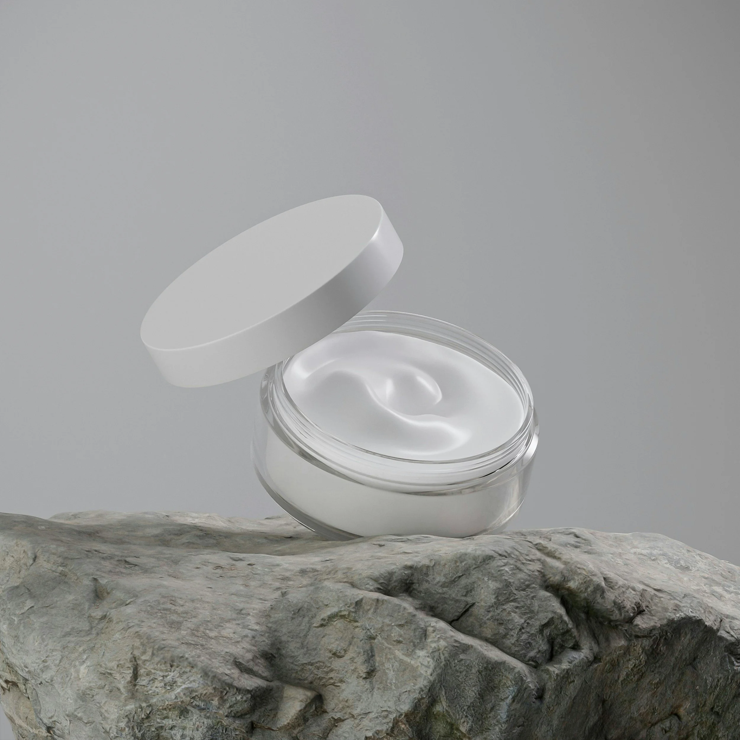 A clear moisturizer jar laying on a flat, textured stone surface.