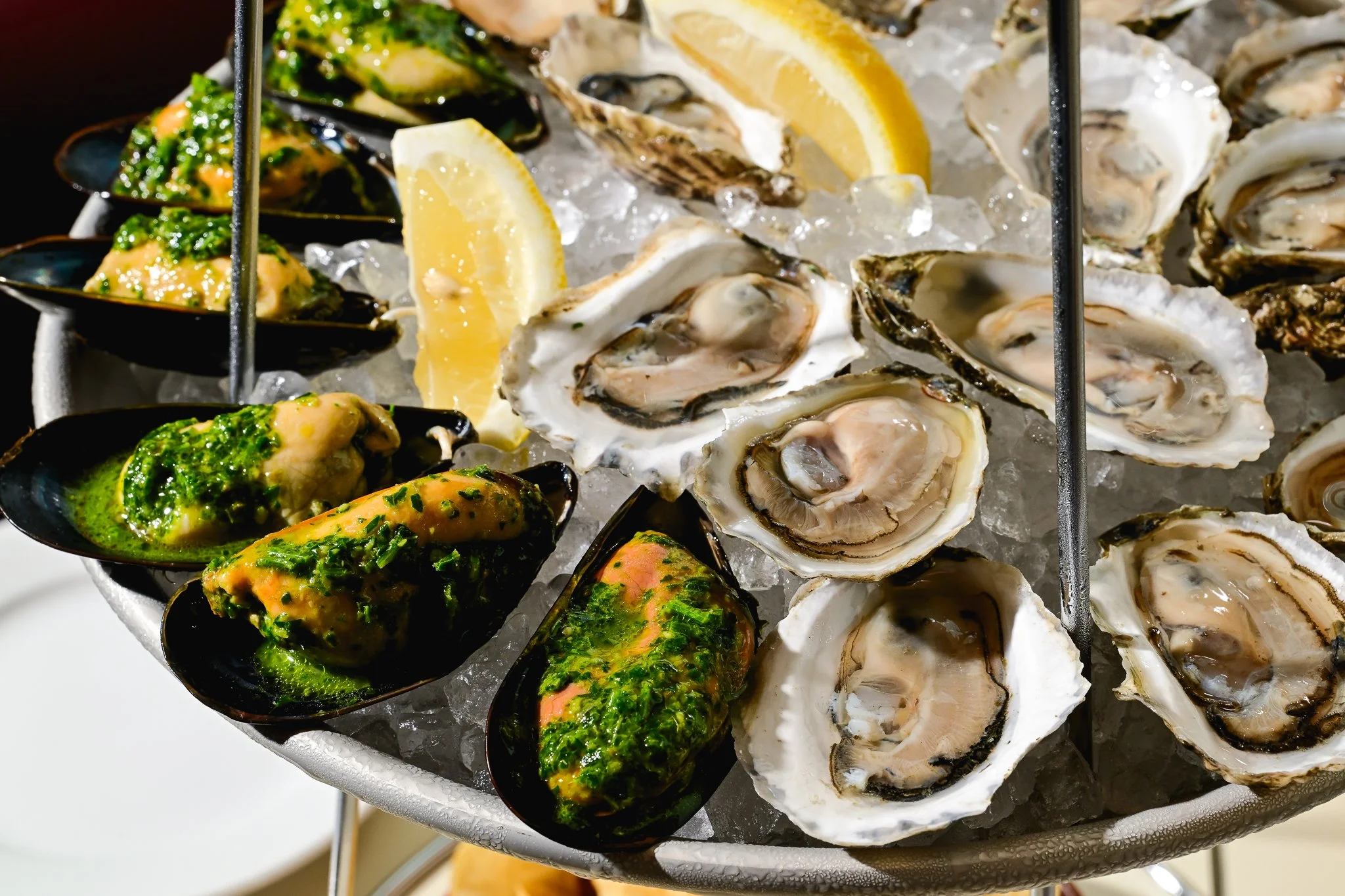 A platter of fresh oysters on ice with lemon wedges and mussels with green parsley sauce.