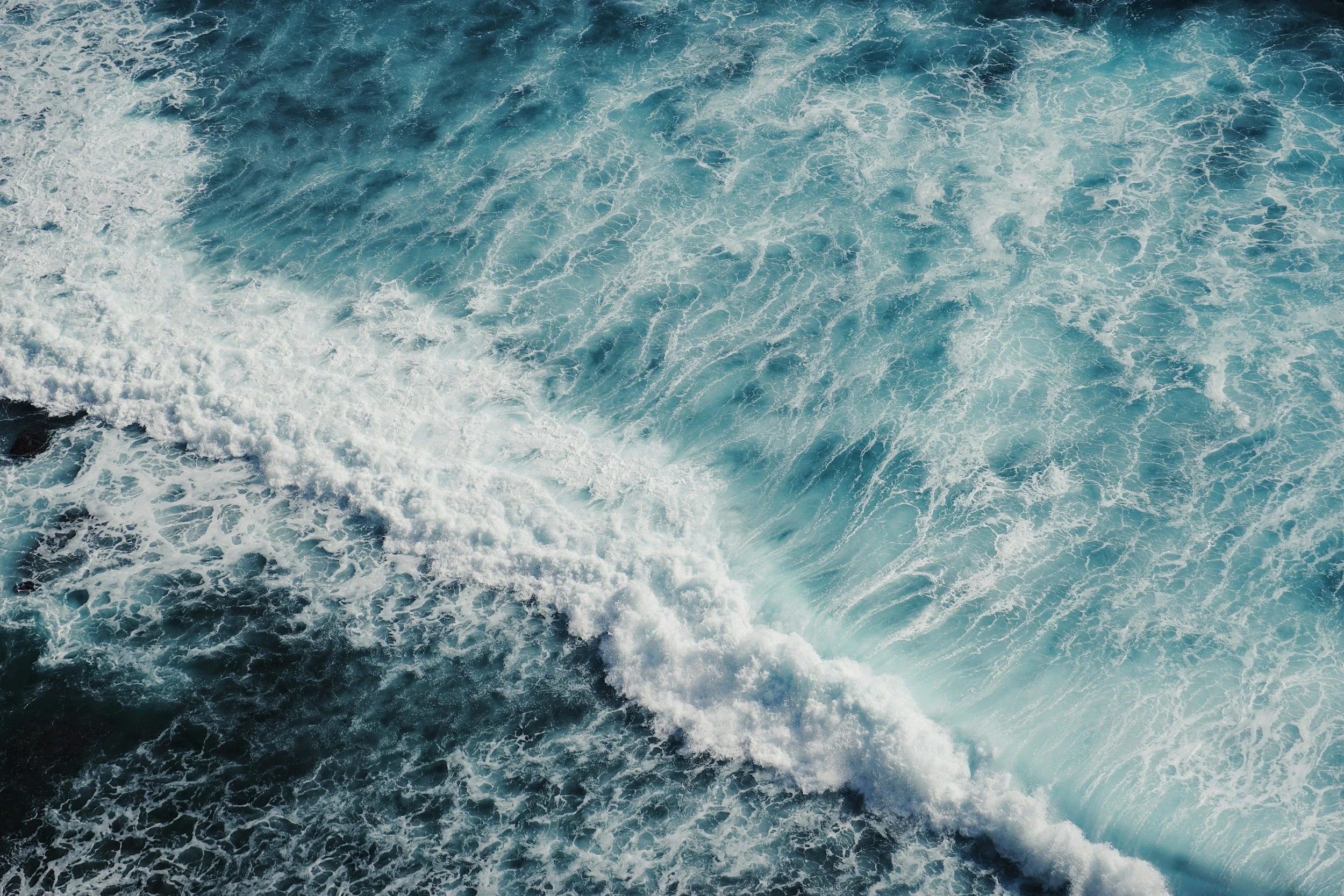 Aerial view of ocean waves with white foam and blue waters.
