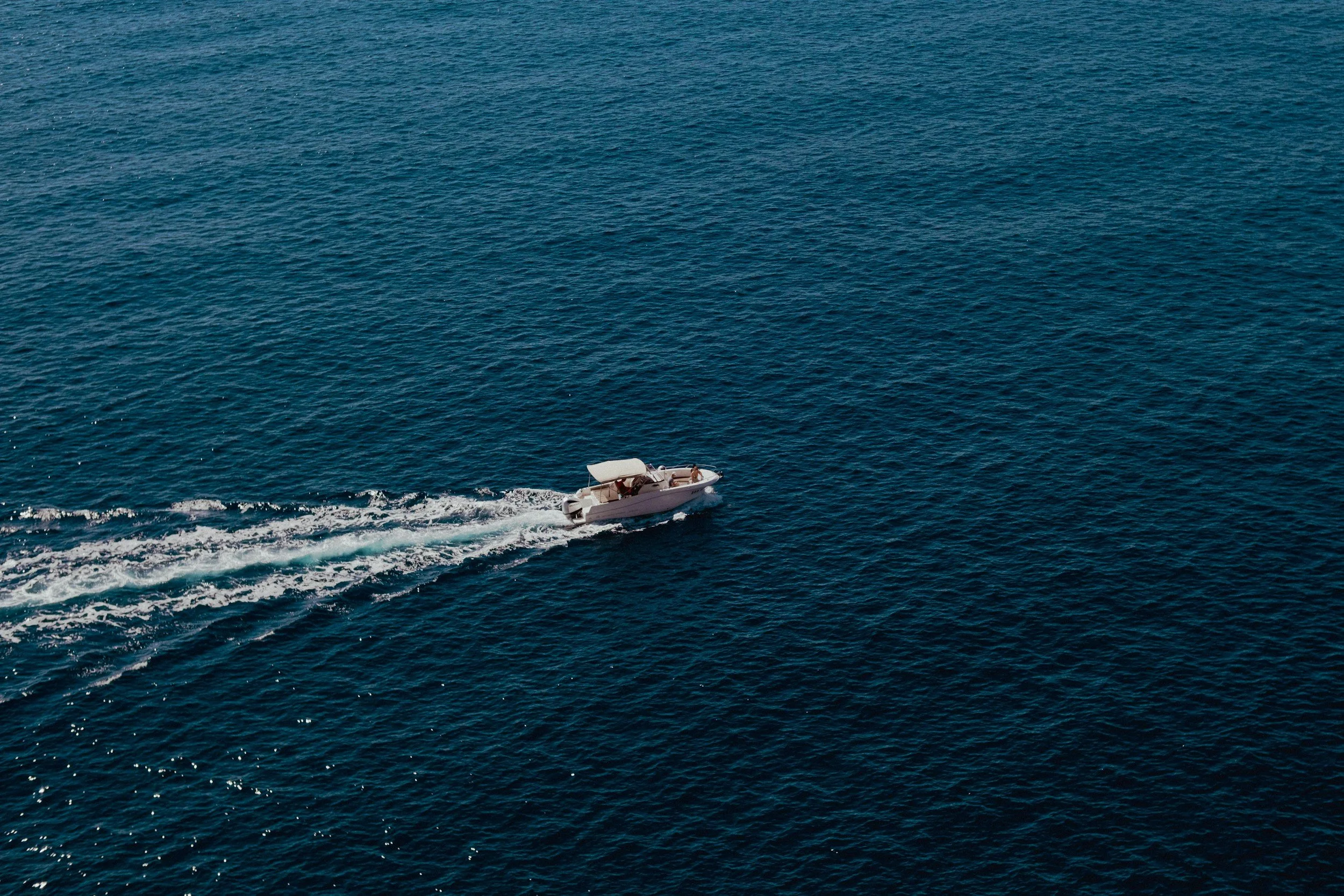 A small white boat with a person on board moving through the ocean, leaving a wake behind.