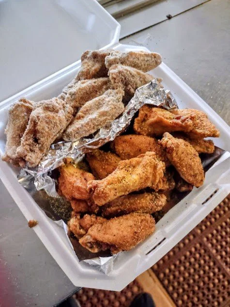 A white takeout container with fried chicken wings and breaded fish fillets, some in aluminum foil.