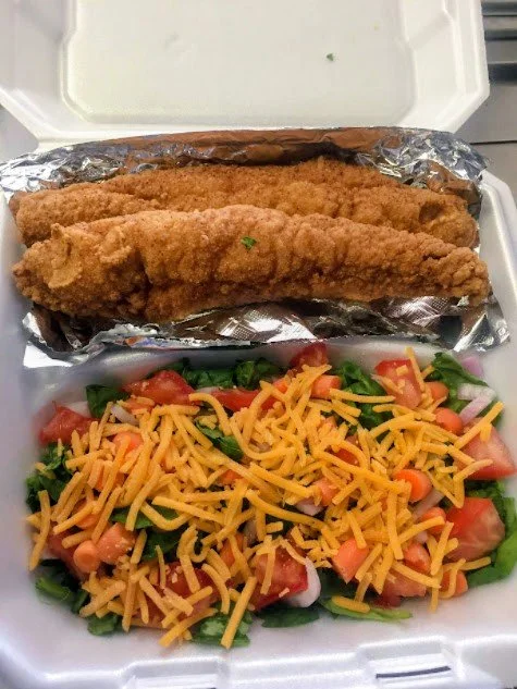 Fried fish fillets and a side salad with shredded cheddar cheese inside a takeout container.