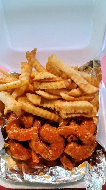 Fast food takeout box filled with crinkle-cut French fries and spicy buffalo chicken bites.
