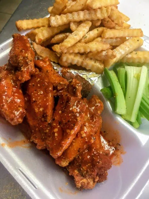 Barbecue chicken ribs with waffle fries and celery sticks on a foam plate.