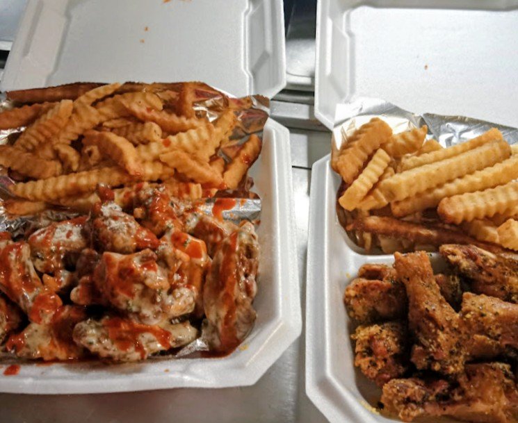 Two foam takeout containers with fried chicken wings, waffle fries, and another crispy chicken portion.