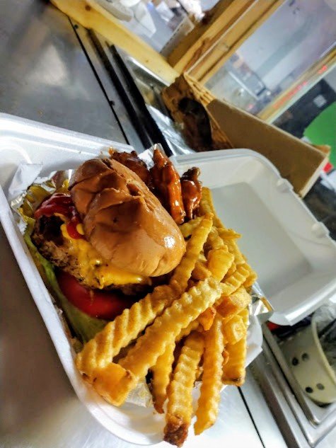 Smoked burger with lettuce, tomato, cheese, and toppings served with crinkle-cut French fries in a takeout container
