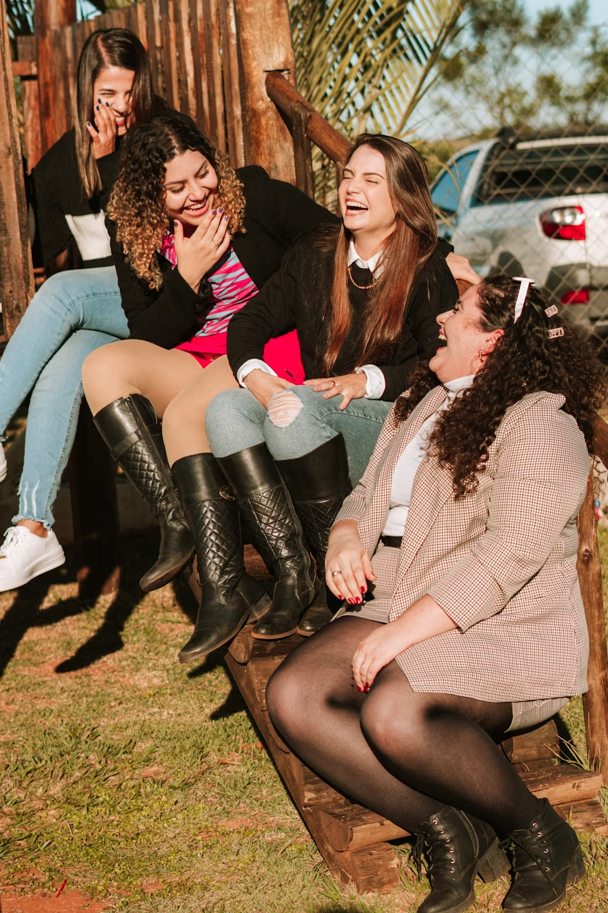Five women sitting on outdoor wooden stairs, laughing and enjoying each other's company.
