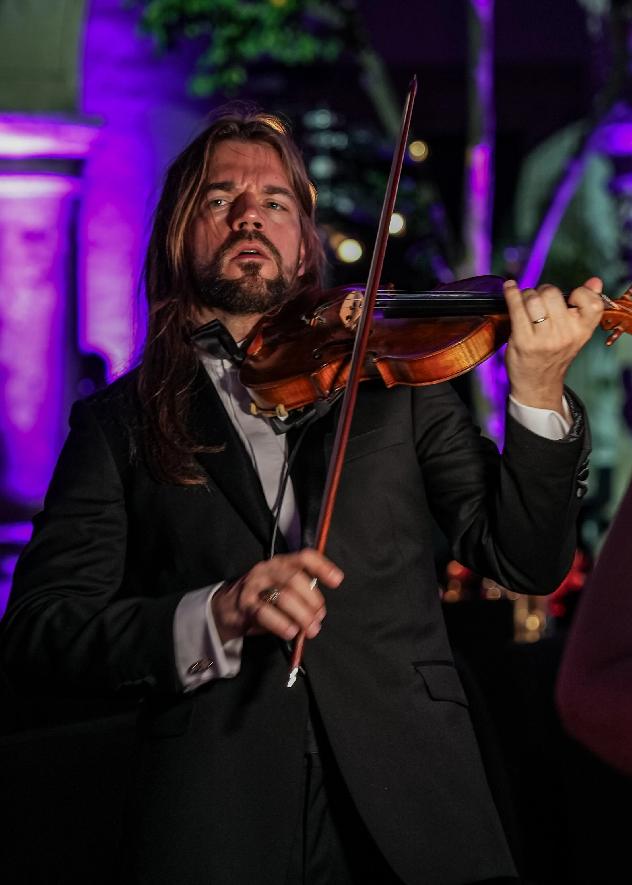 Hombre tocando el violín en un ambiente oscuro con iluminación púrpura y verde. Gala Miss Universo Guadalajara. Palacio de Gobierno. Markus Violin.
