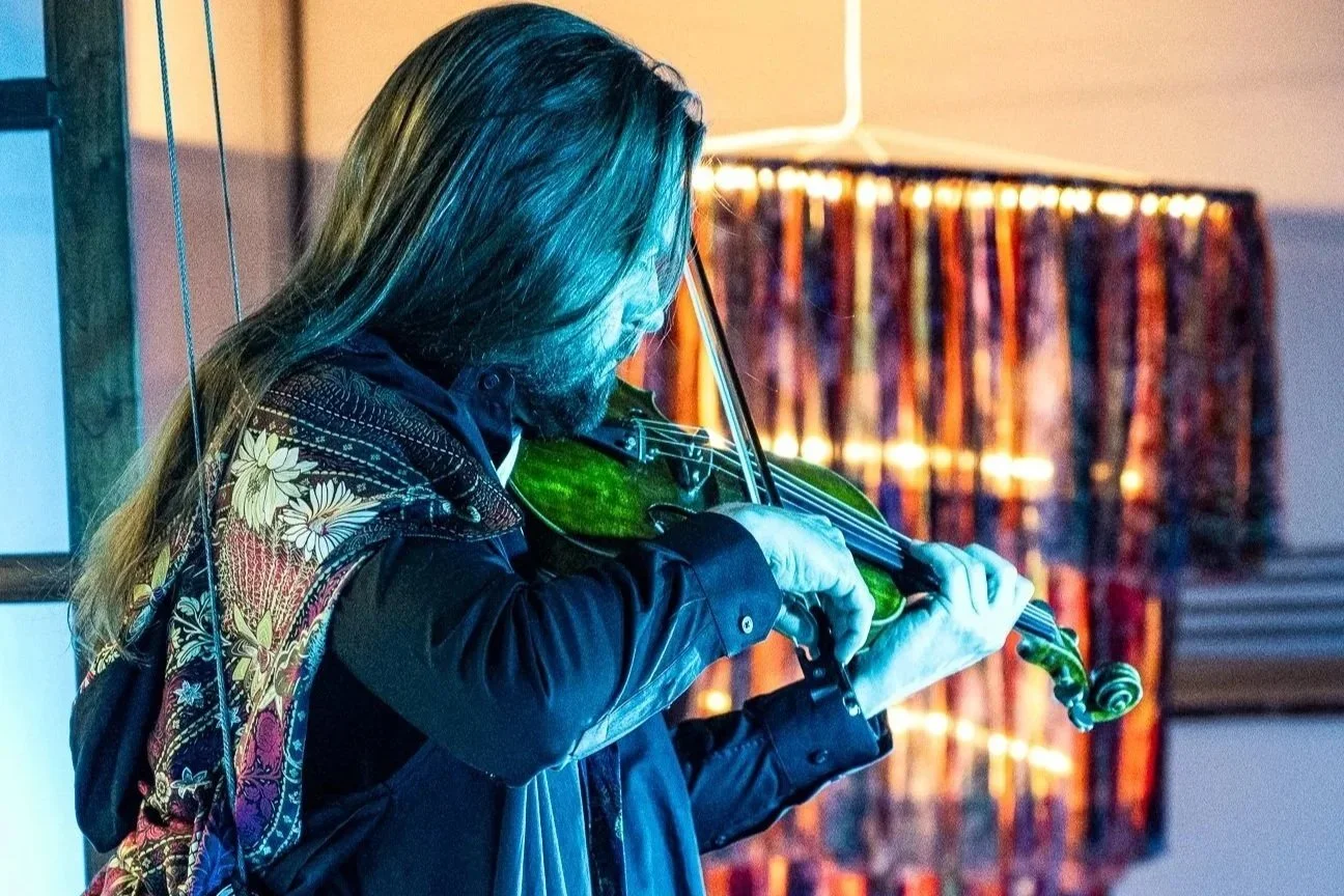 Markus tocando violín en un ambiente interior con iluminación suave y fondo con cortinas y lámpara. MUPE, CDMX. Pineda Covalin.