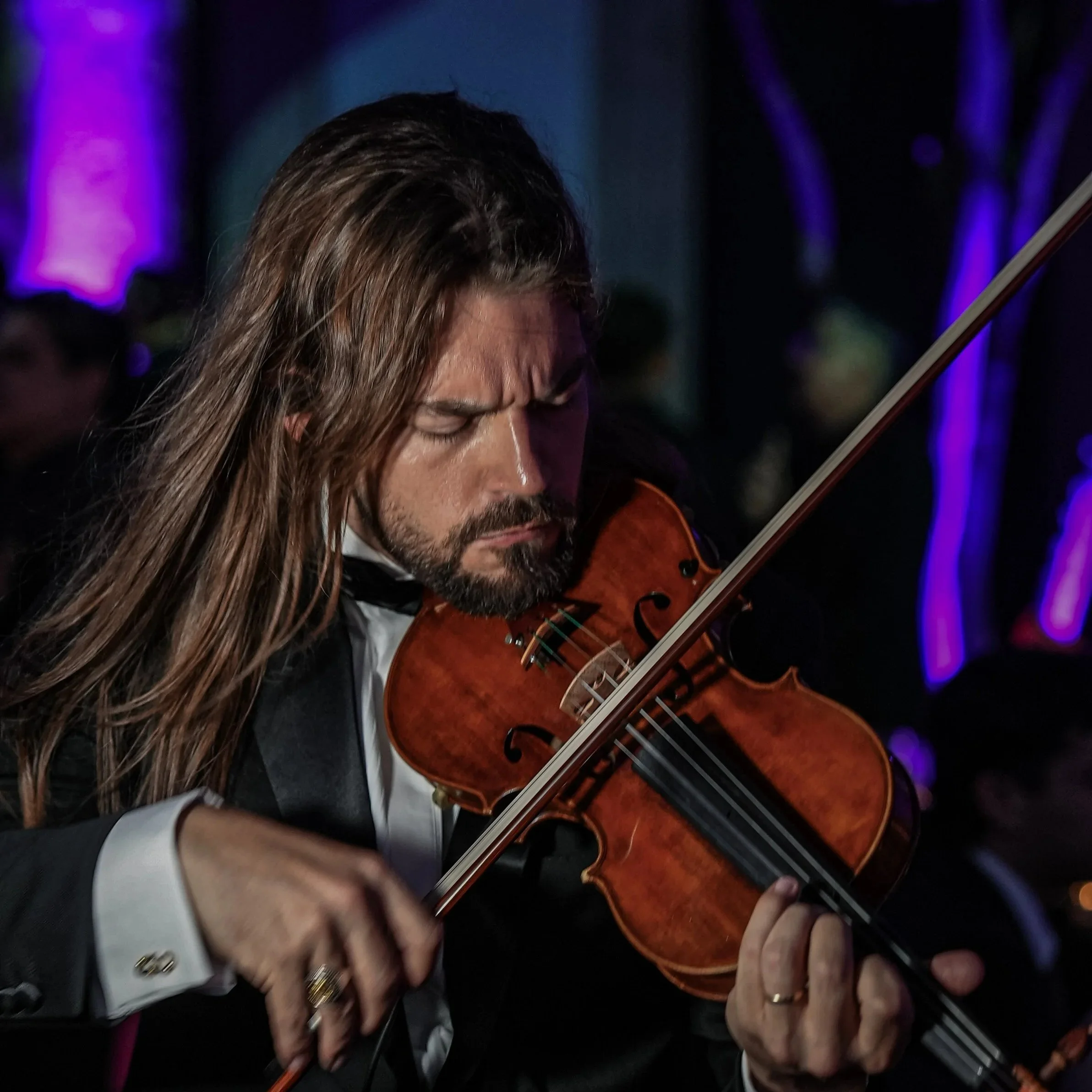 Markus hombre tocando violín en un escenario con luces púrpuras y negras, fue principalmente en Guadalajara, en el evento de la Gala de miss universo, 2025.