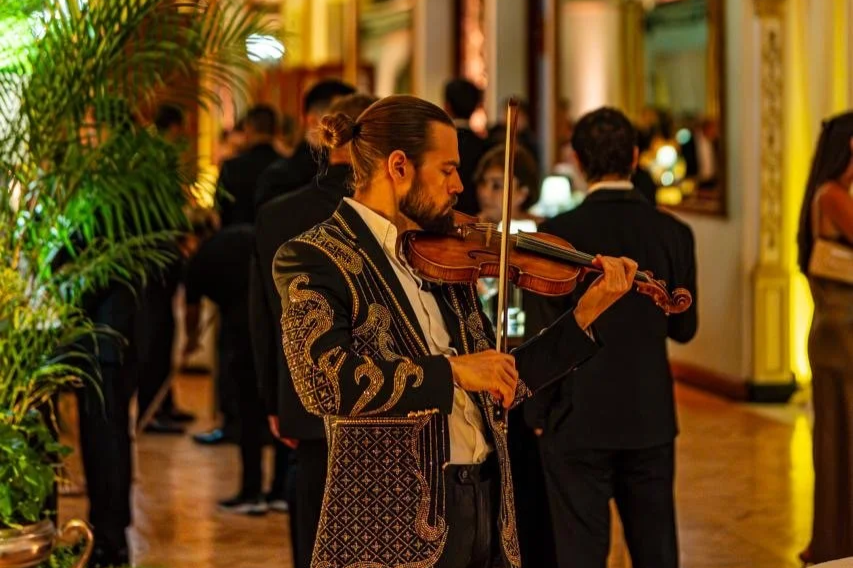 Hombre, Markus tocando violín en una fiesta elegante con personas vestidas de gala en el fondo. Casino Español, Ciudad de México. CDMX