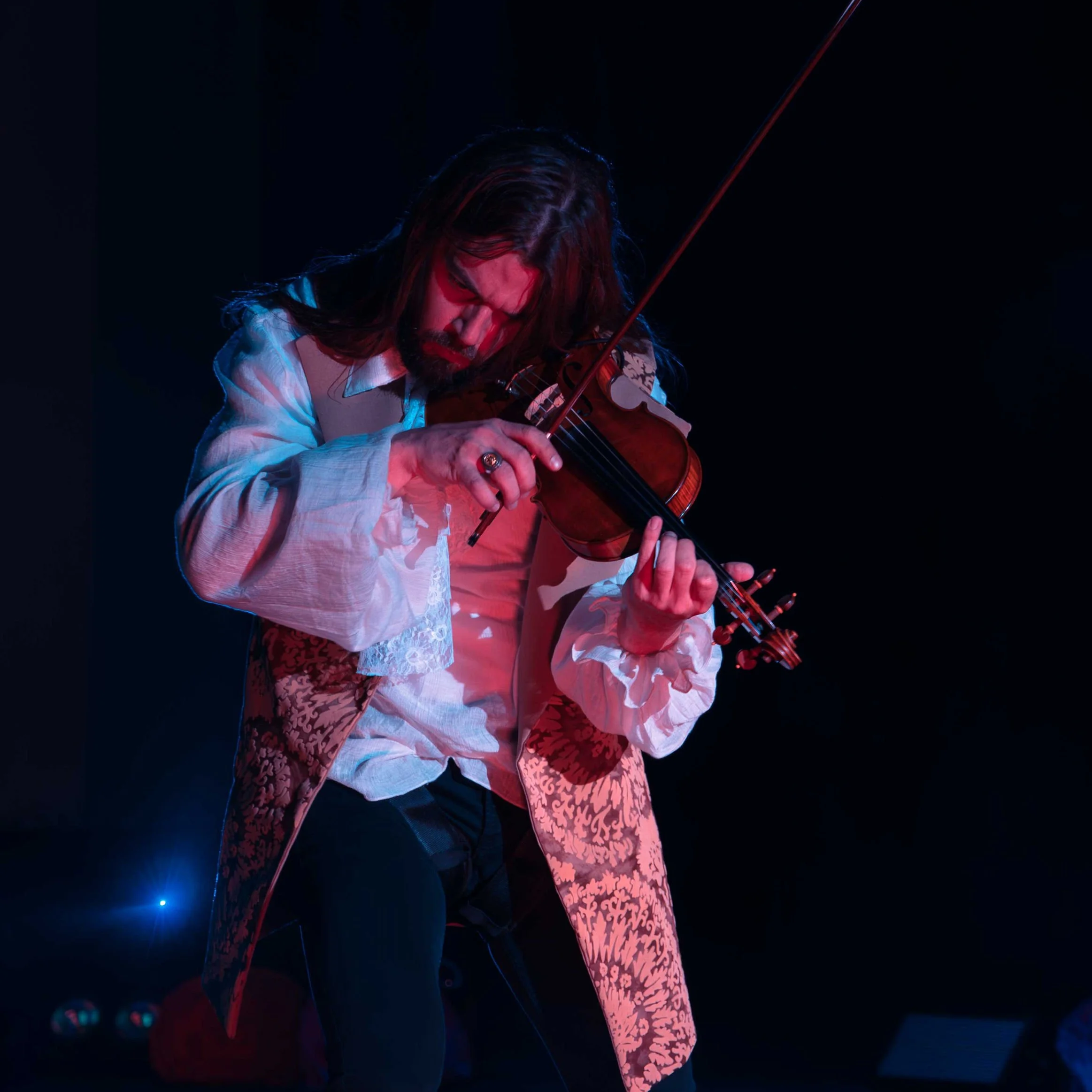 Hombre tocando violín en un escenario oscuro con iluminación de colores rojos y azules. Interpretación de obra de violinista. Show violinista en Teatro de la Alcaldía Alvaro Obregón. Markus Violin.