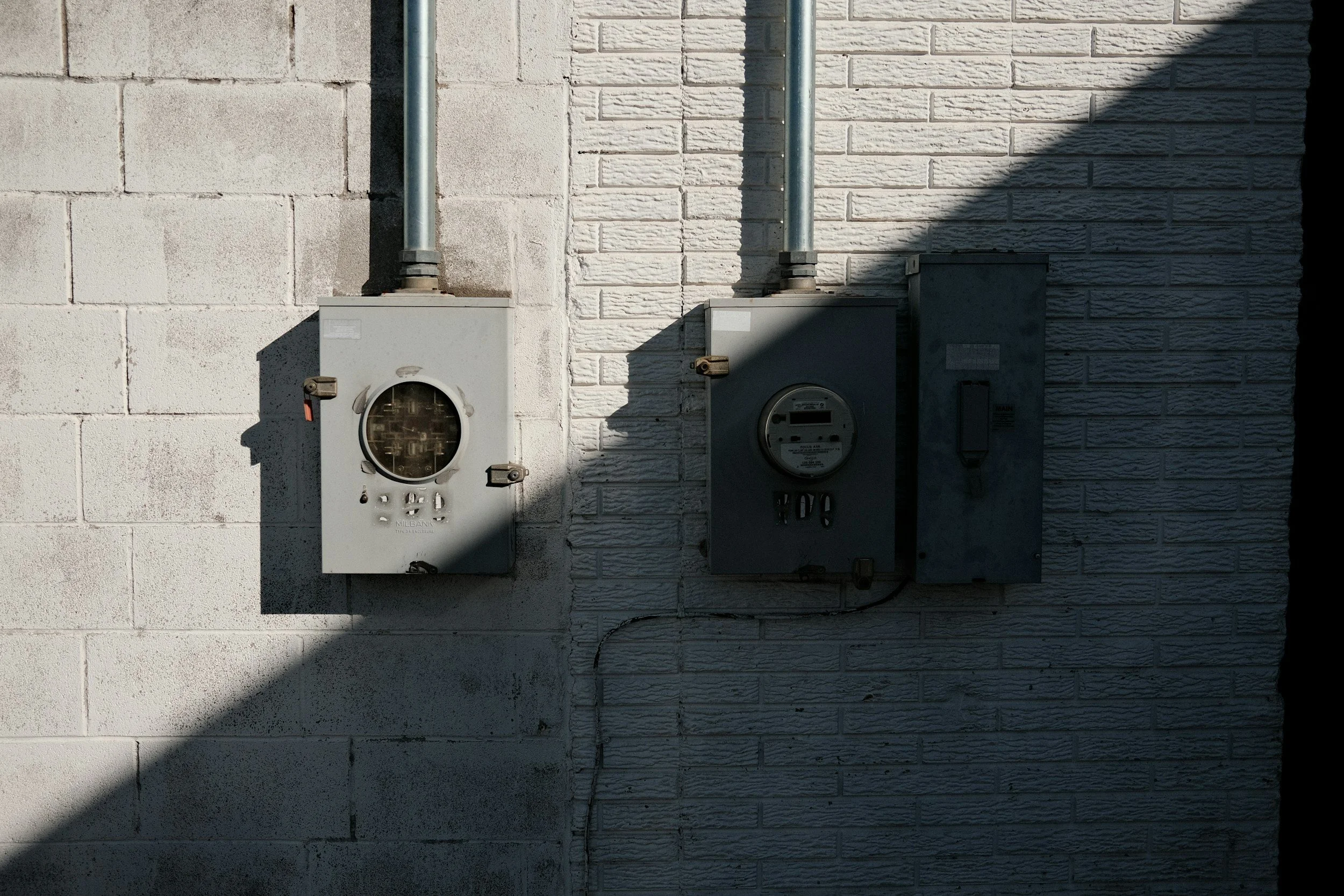 Close-up of two electrical meters mounted on a brick wall, with shadows cast across the wall and meters.
