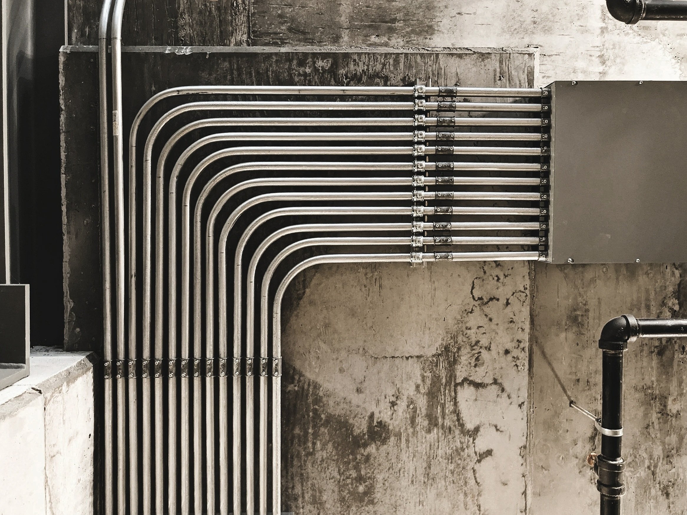 A set of exposed metallic pipes arranged vertically against a concrete wall in an industrial setting.