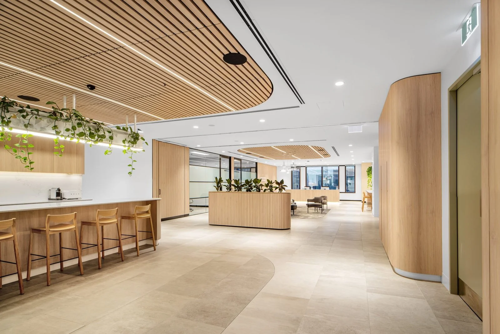 Modern office interior with wooden panels, a reception area with potted plants, and seating arrangements near large windows.