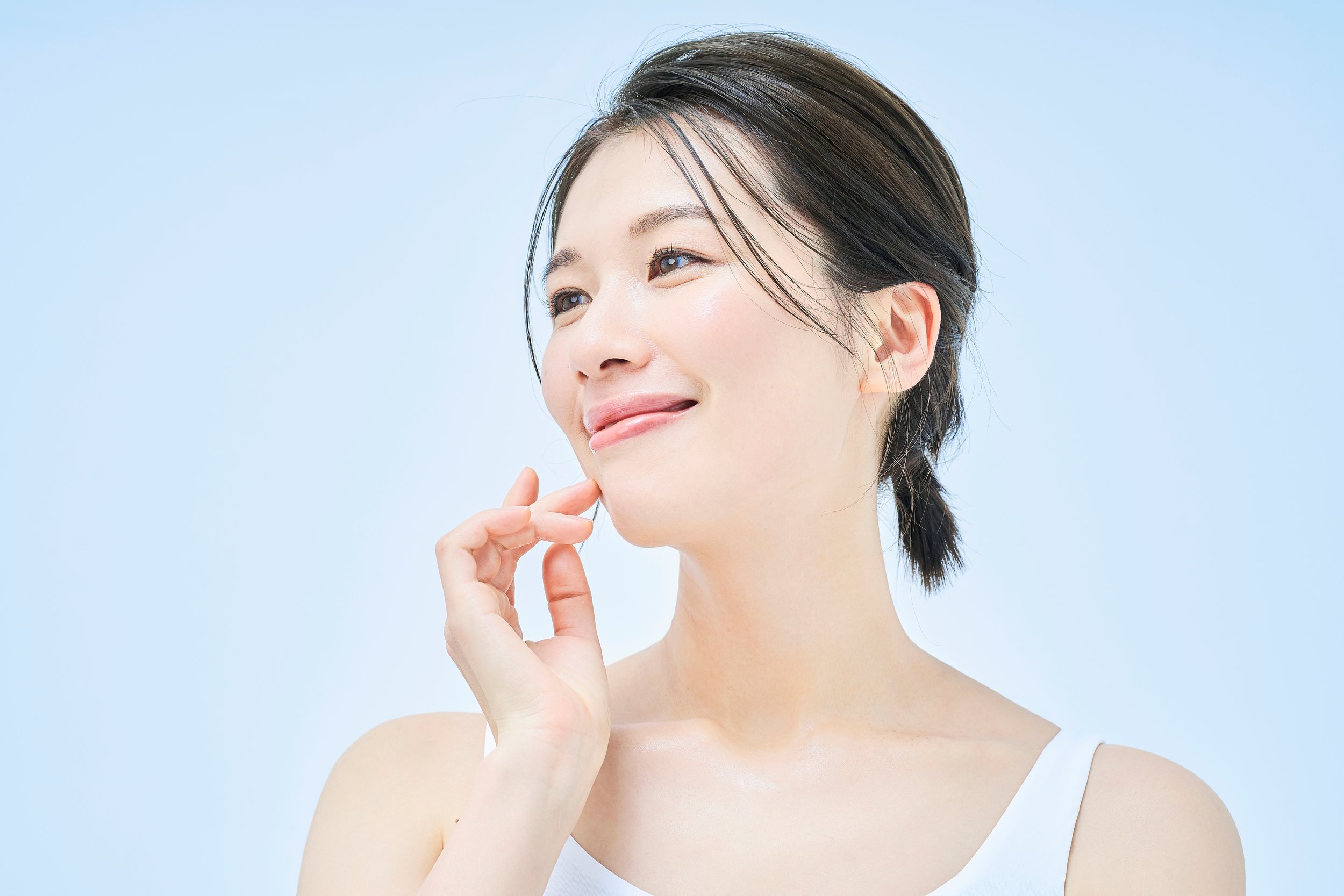 A smiling woman with short, dark hair and blue eyes, touching her chin with her hand, against a light blue background.