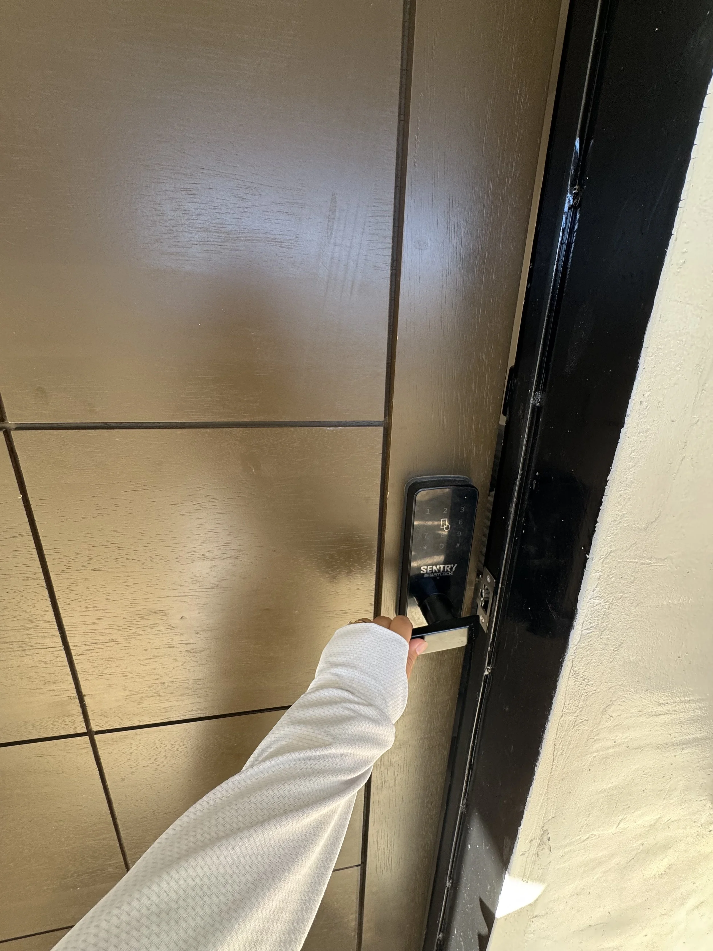 A person with a white sleeve is pressing a digital lock keypad on a elevator door.