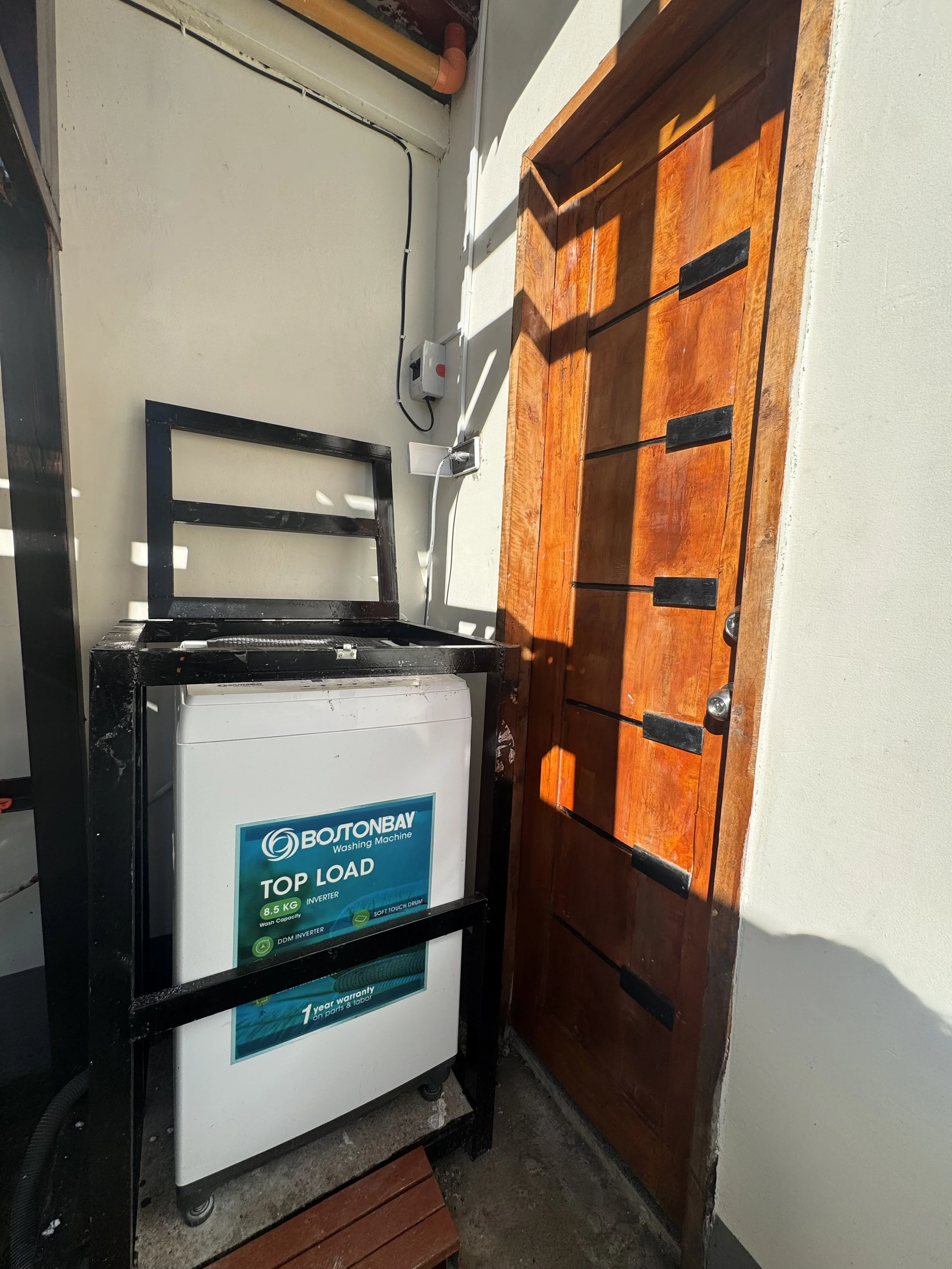 A washing machine with a sign indicating it's a top load model with an 8.5 kg capacity, placed next to a wooden cabinet in a laundry area.