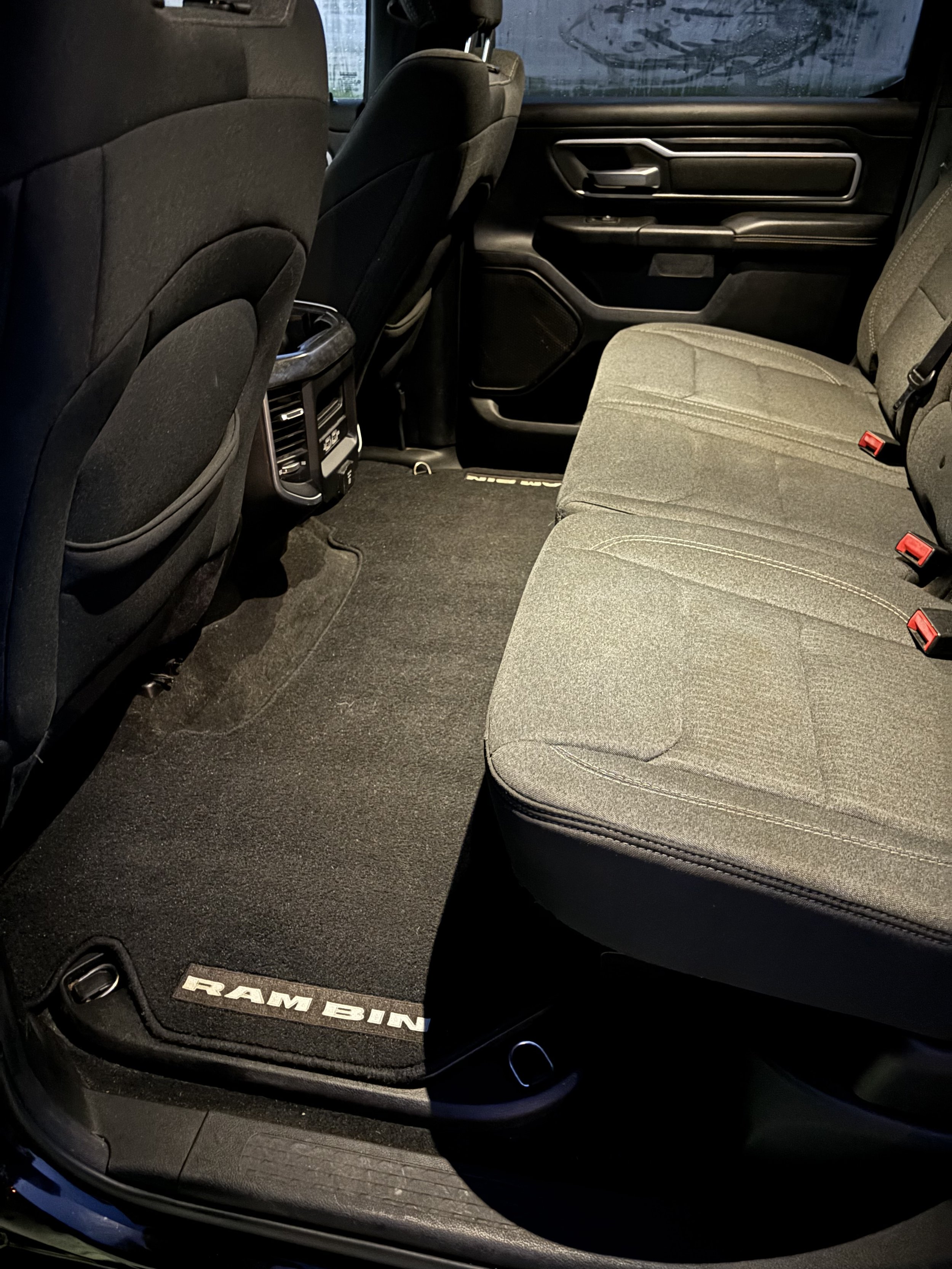 The interior of a Ram Bighorn truck showing black fabric seats, floor mats, and dashboard with rear passenger air vents.