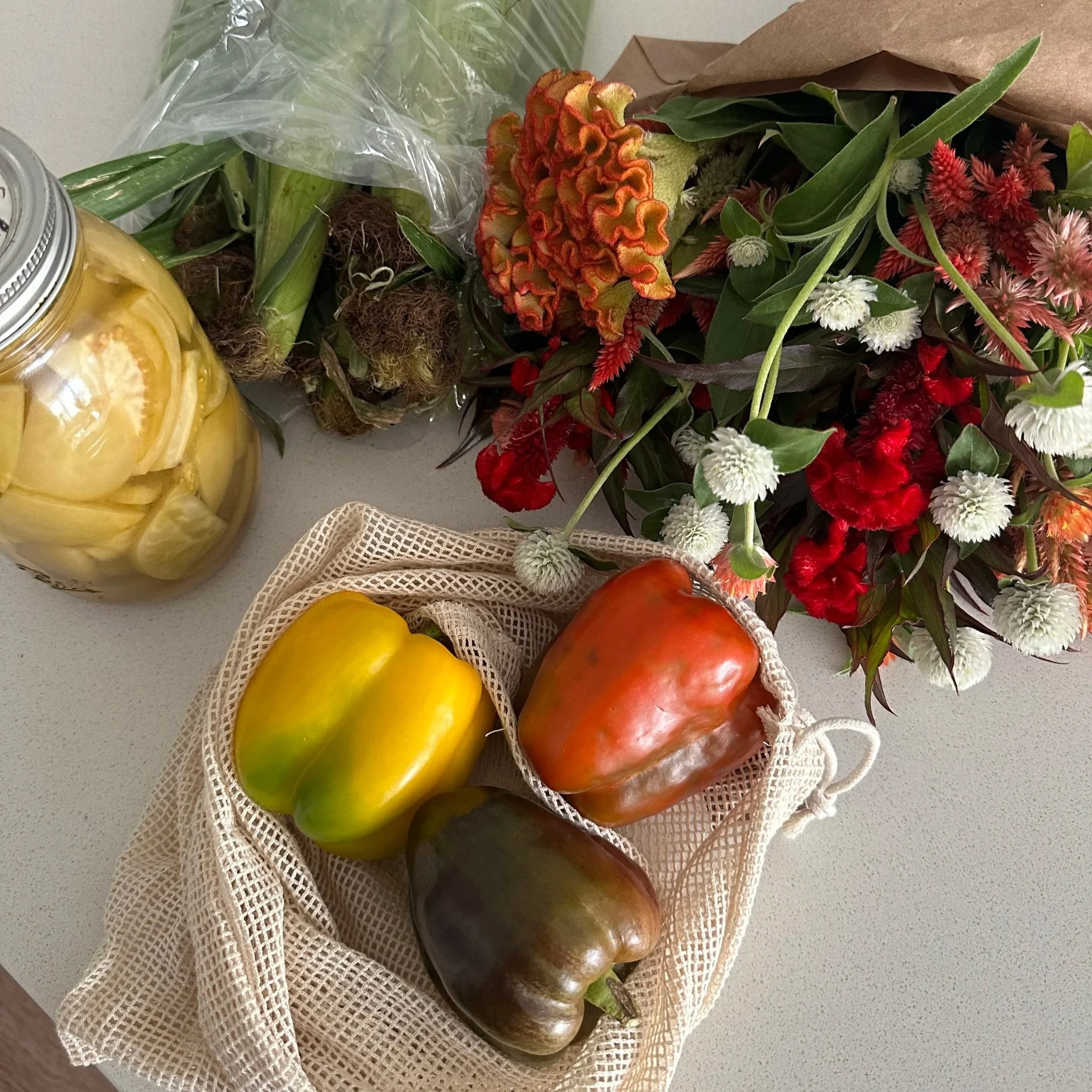 Various fresh fruits and flowers, including apples, a yellow melon, and a bouquet of mixed red, white, and orange flowers on a light-colored surface.