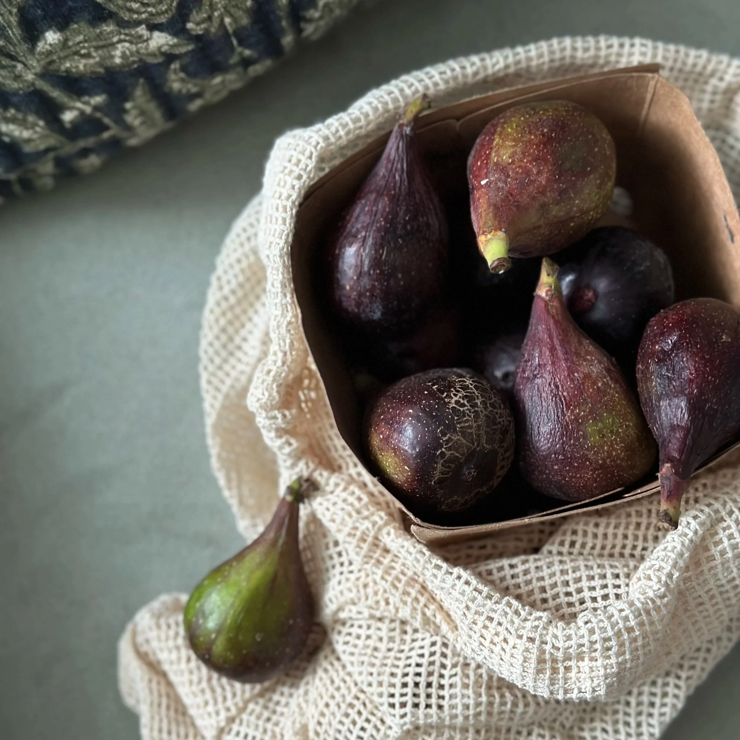 A cloth bag containing fresh figs on a vintage suede chair.