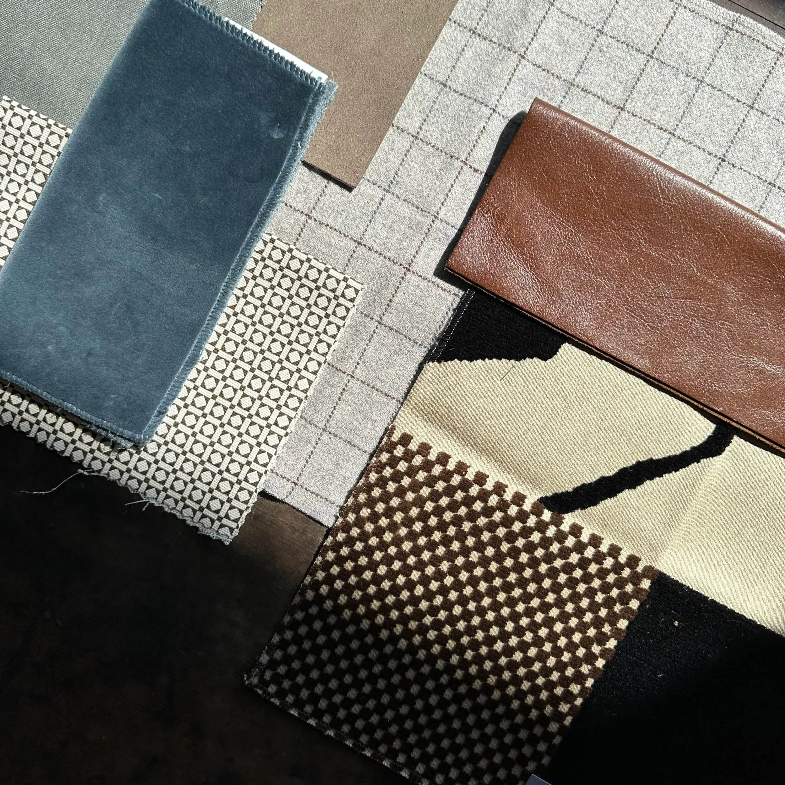 A collection of fabric and material samples arranged on a surface, including patterned, solid, and textured fabrics in various colors like beige, brown, black, gray, and blue.