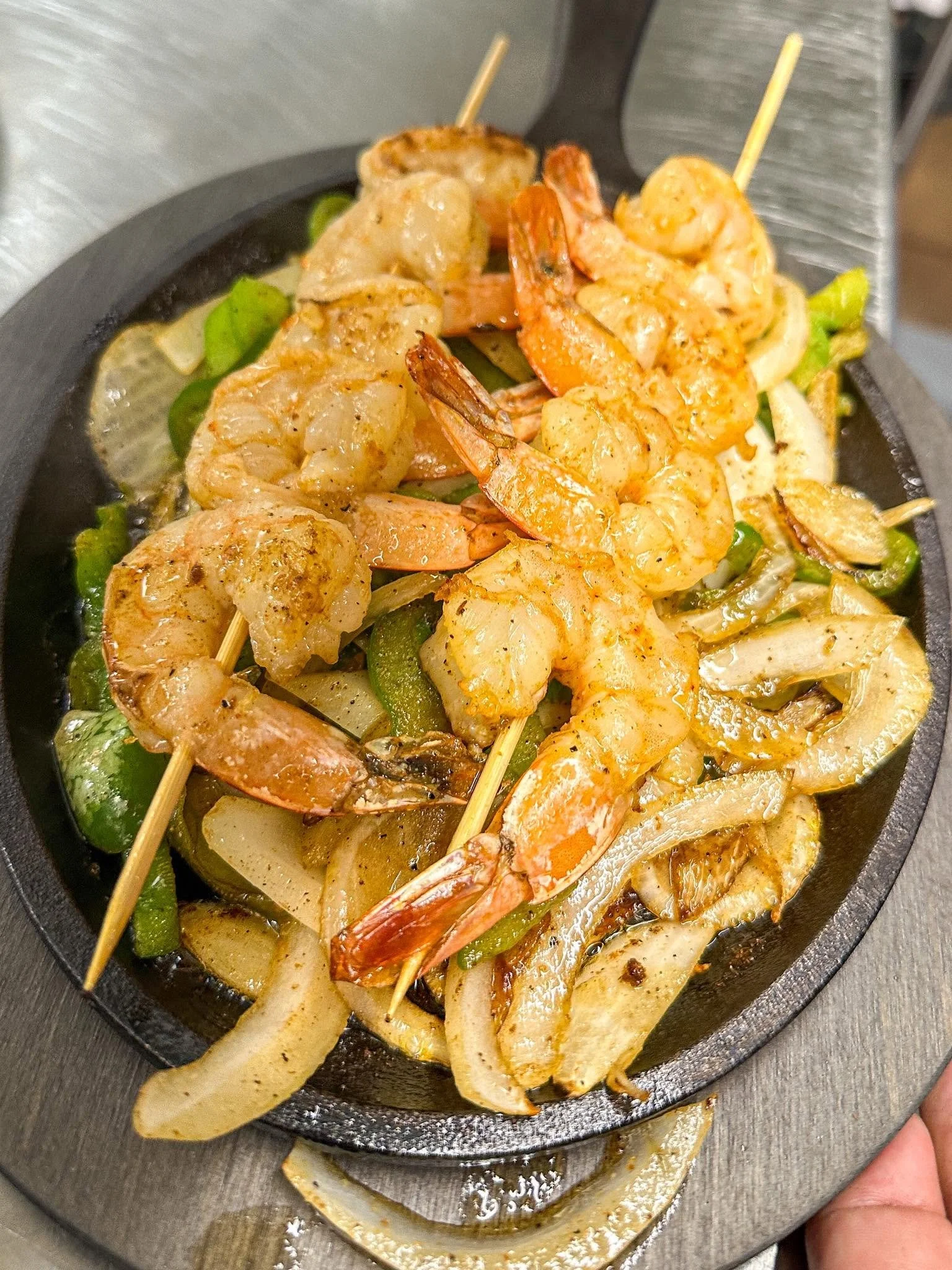 Skewers of grilled shrimp and chicken on a hot cast iron skillet with vegetables.